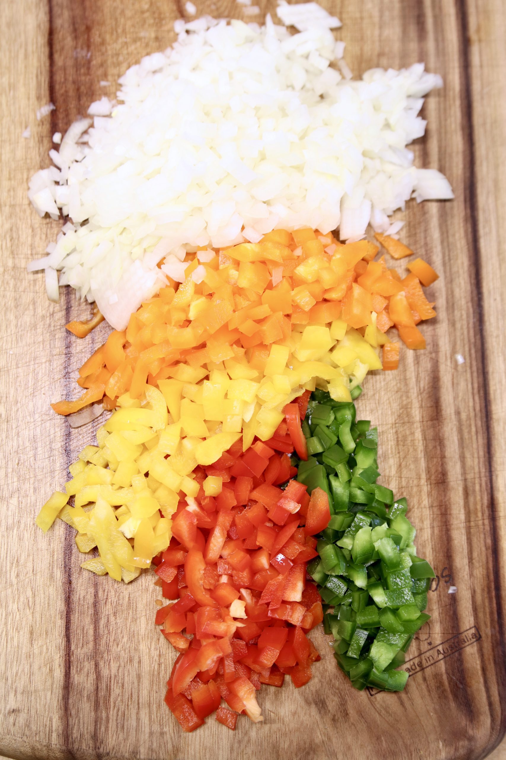 diced onions, orange, yellow, red and green bell peppers on a cutting board