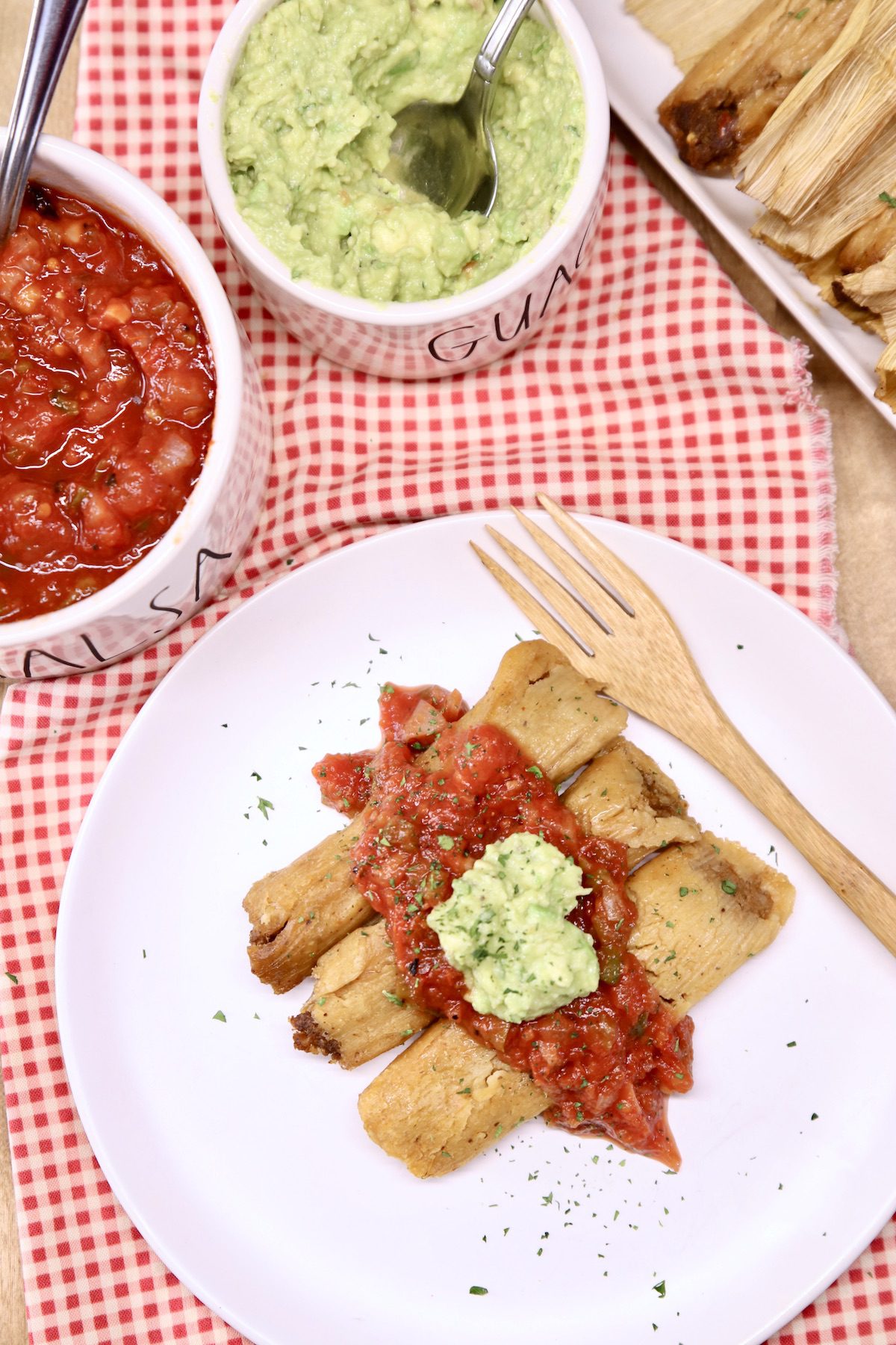 overhead of plate of tamales with salsa and guacamole