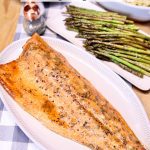 whole salmon filet on a platter, asparagus and rice dish in background.