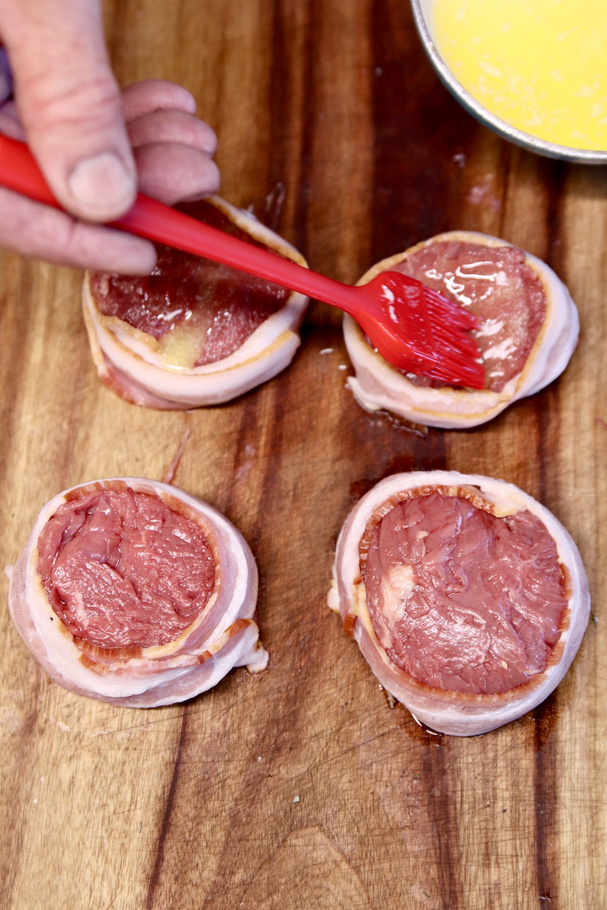 brushing butter over bacon wrapped tenderloin steaks