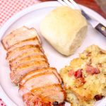 Best Marinated Pork Chops - sliced on a plate with potatoes & dinner roll.