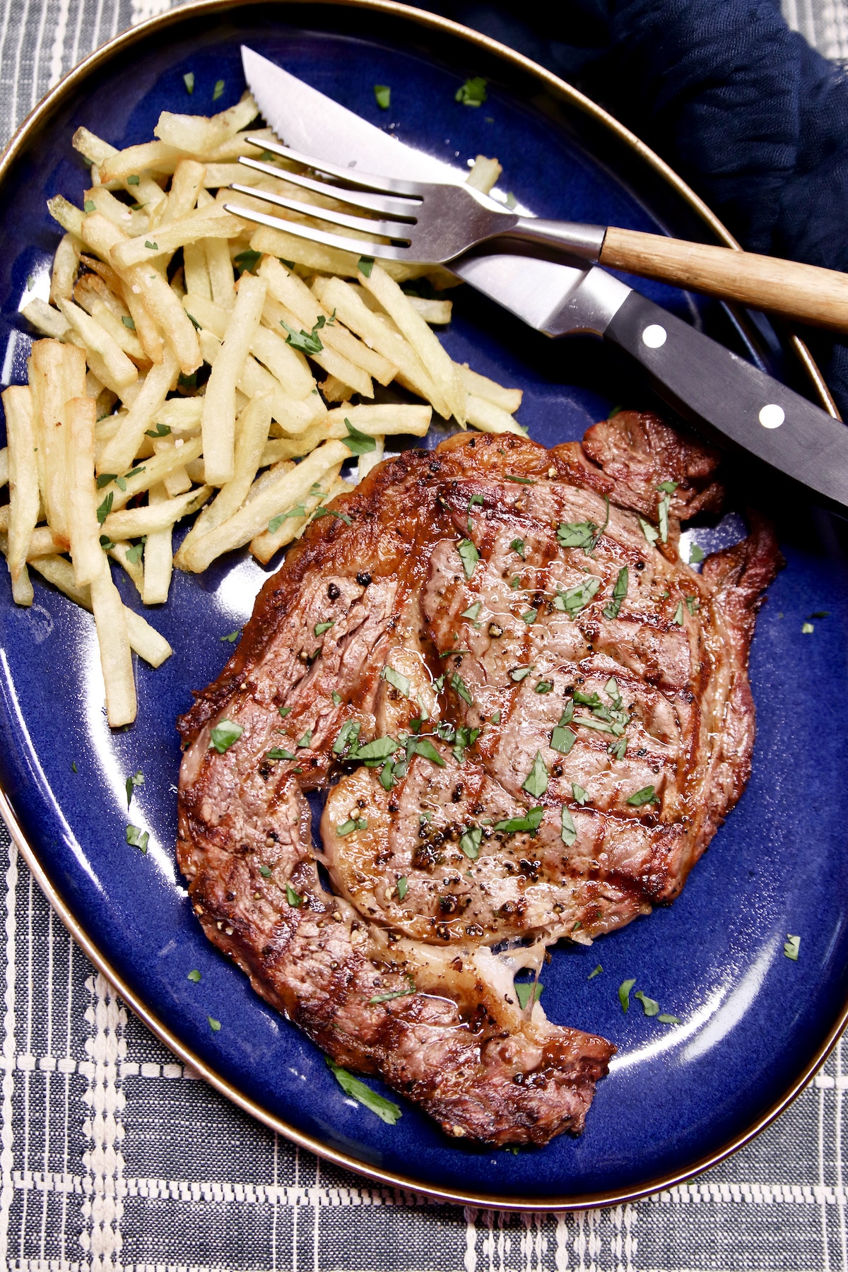 Grilled steak and fries on a blue platter, fork & knife.