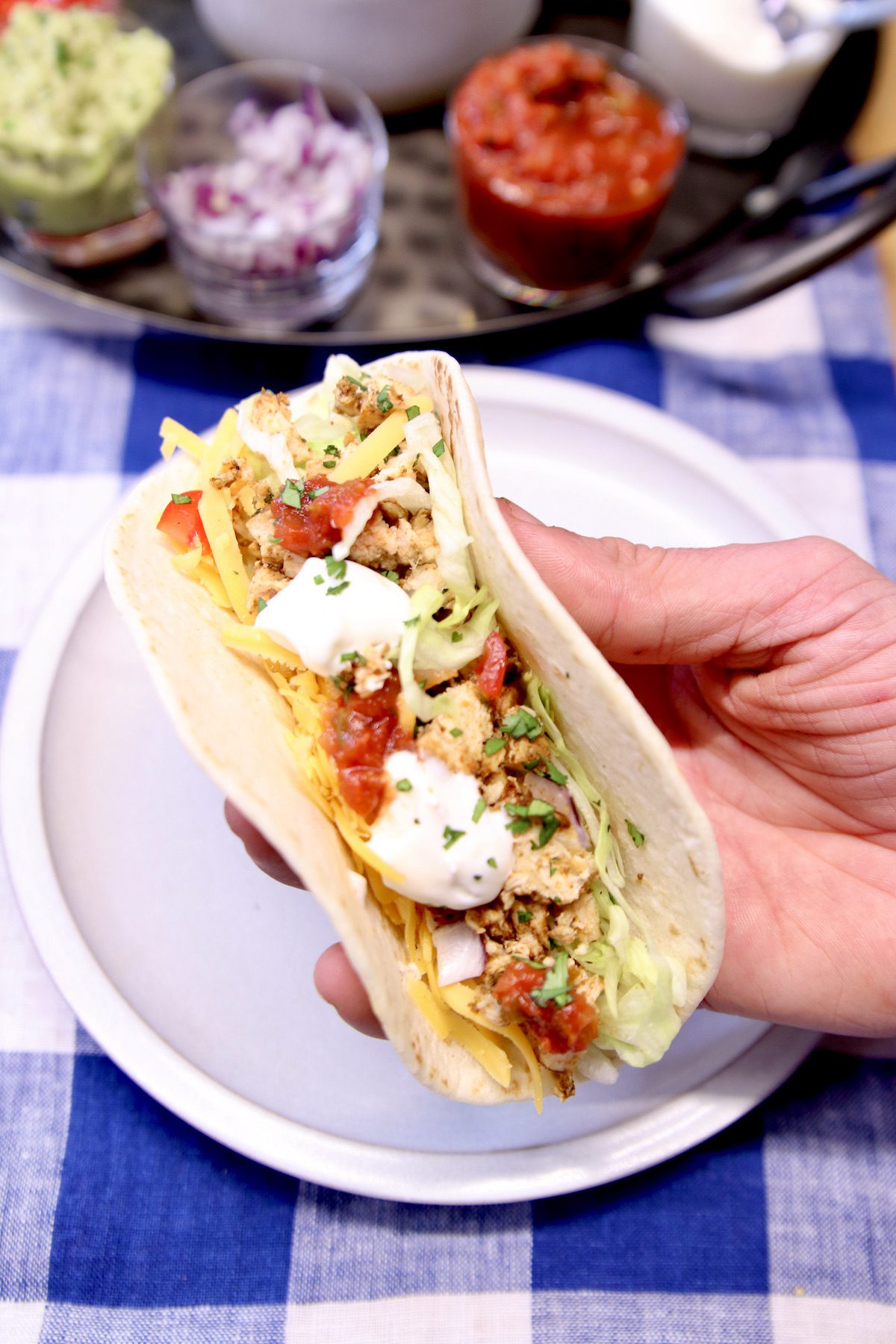 hand holding a chicken soft taco with sour cream and salsa