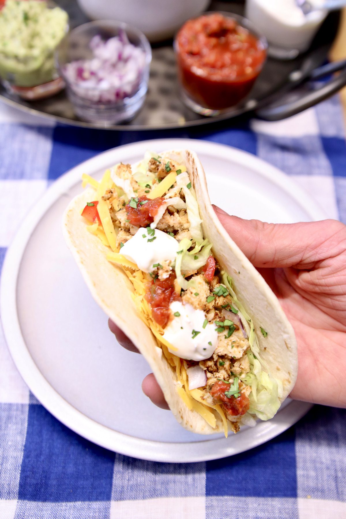 hand holding soft taco over a plate with chicken, sour cream, salsa