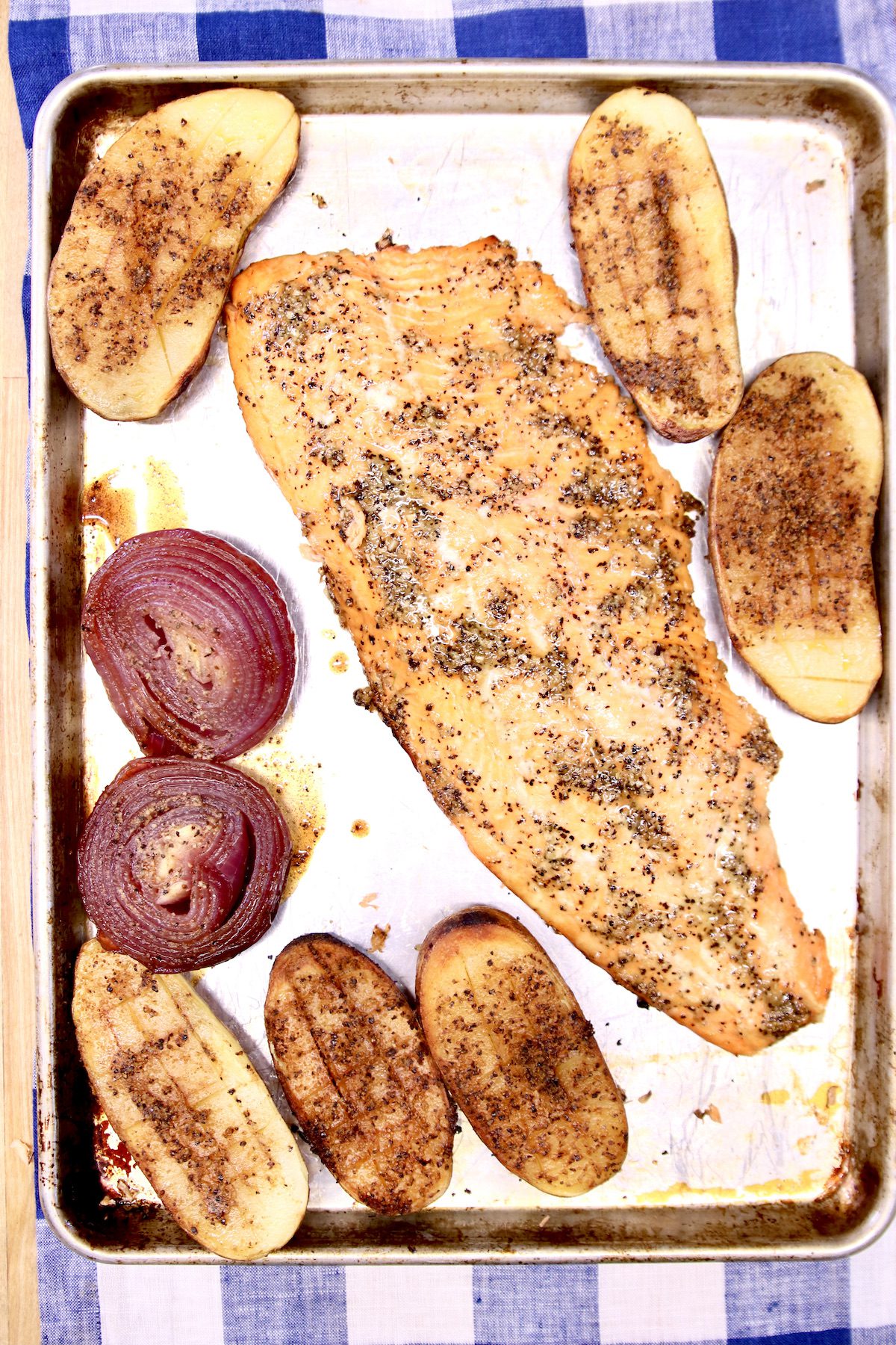 grilled salmon fillet on a sheet pan with baked potato halves and red onion.