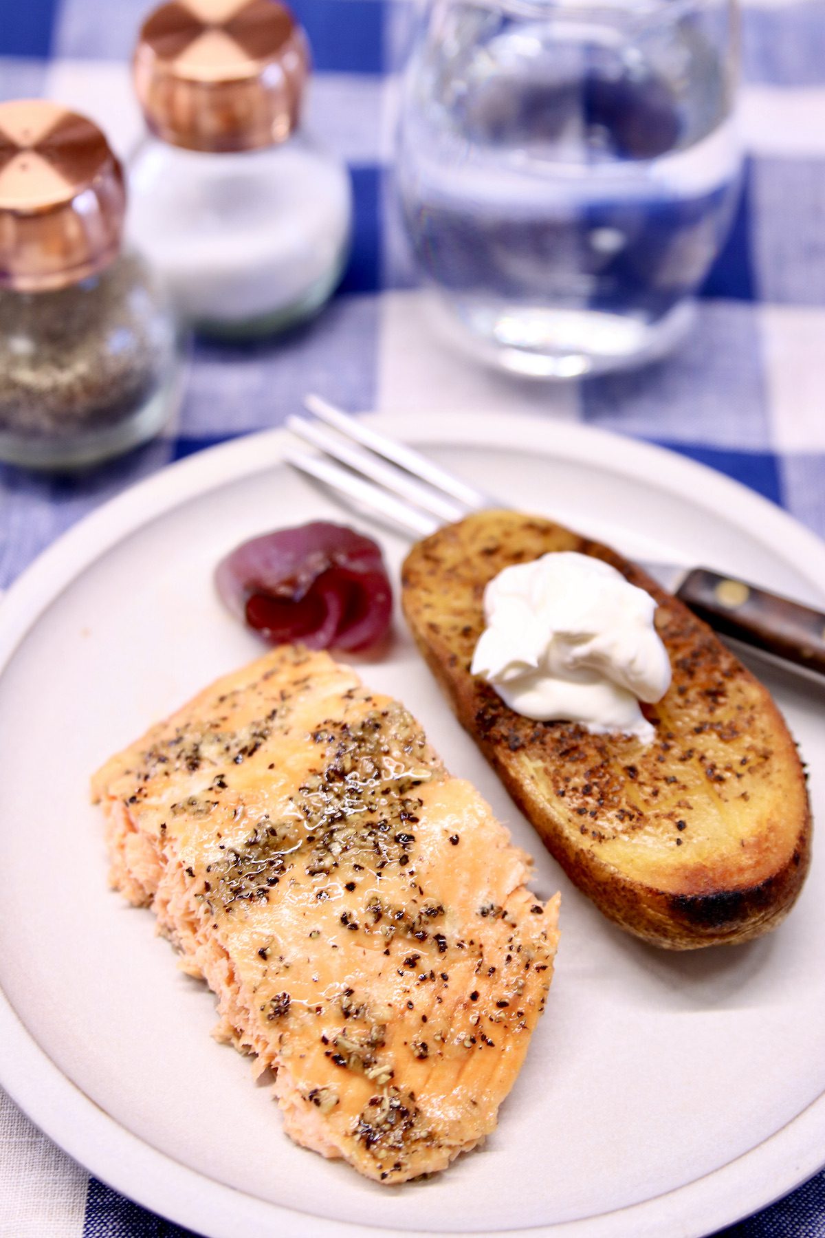 grilled salmon fillet on a plate with ½ of a baked potato with sour cream.