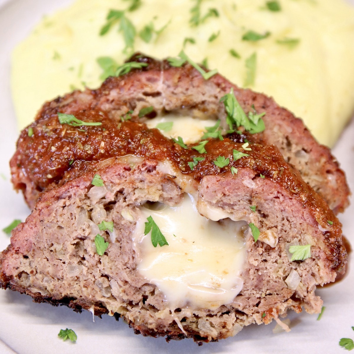 2 slices of mozzarella stuffed meatloaf on a plate with mashed potatoes.