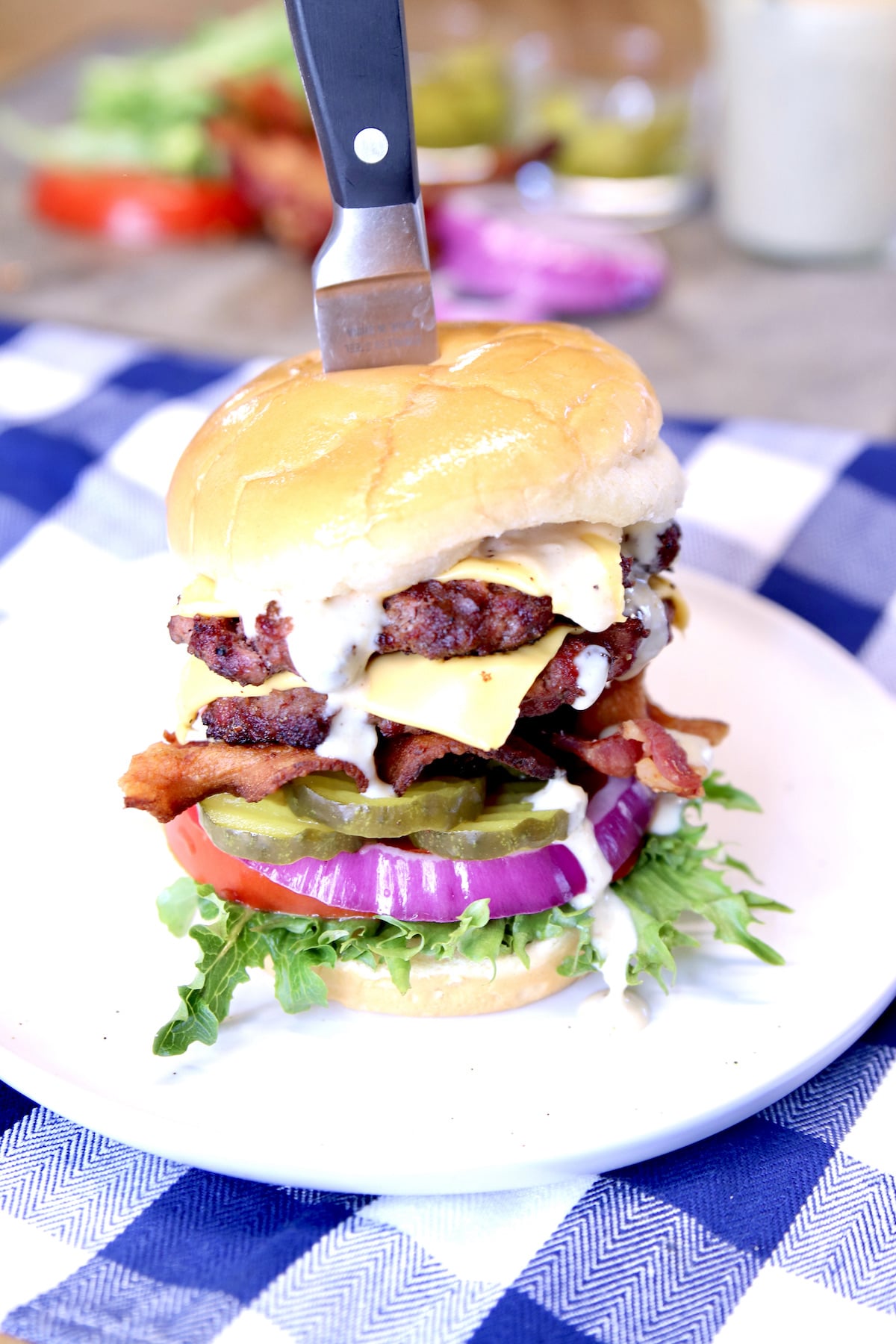 Bacon double cheeseburger on a plate with white bbq sauce, pickles, tomato, red onion.