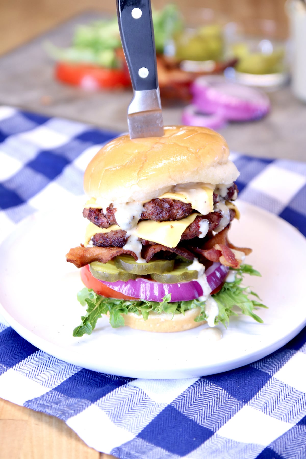 grilled double cheeseburger with bacon on a plate. Knife stuck through the burger.