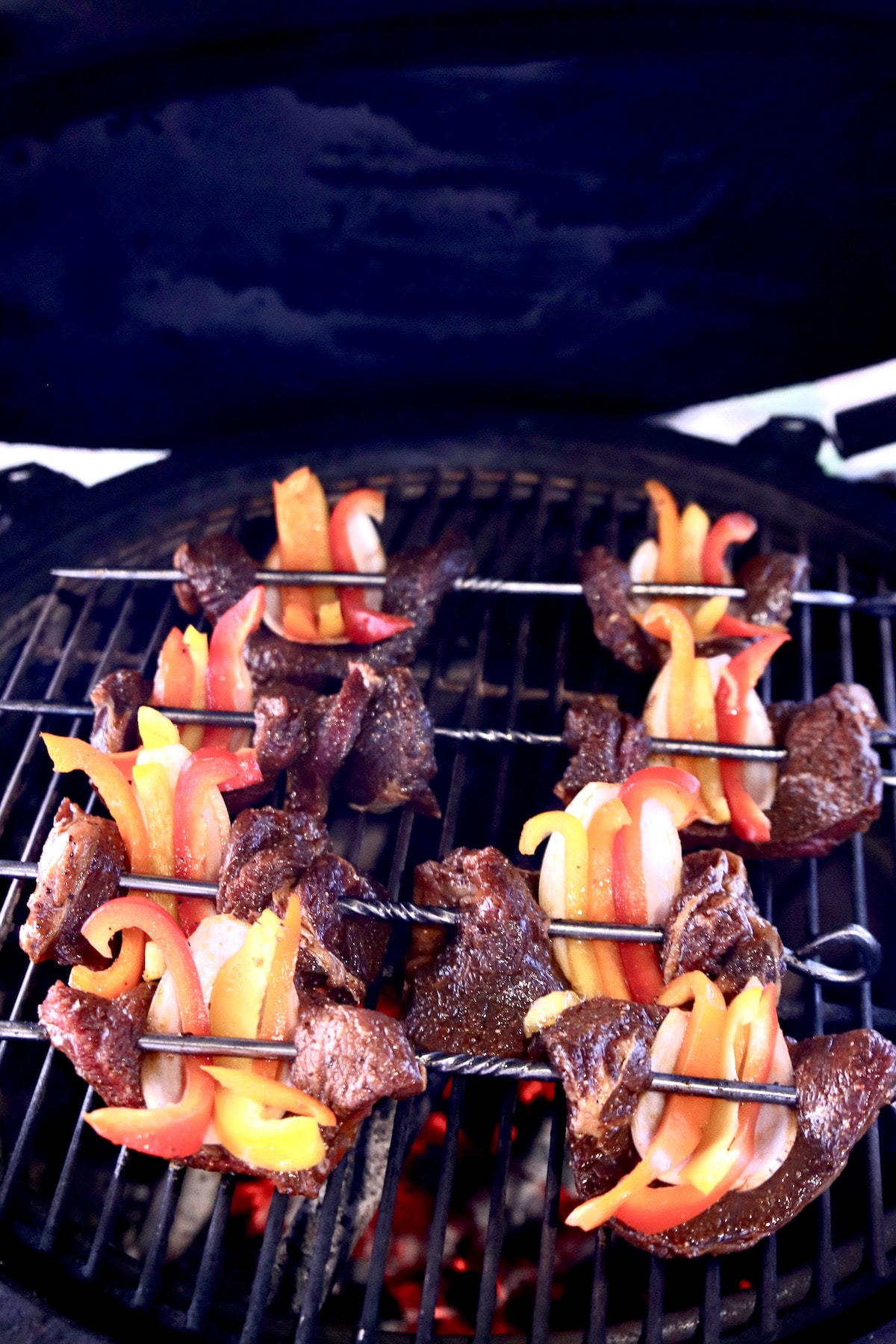 marinated steak skewers with peppers and onions on grill.