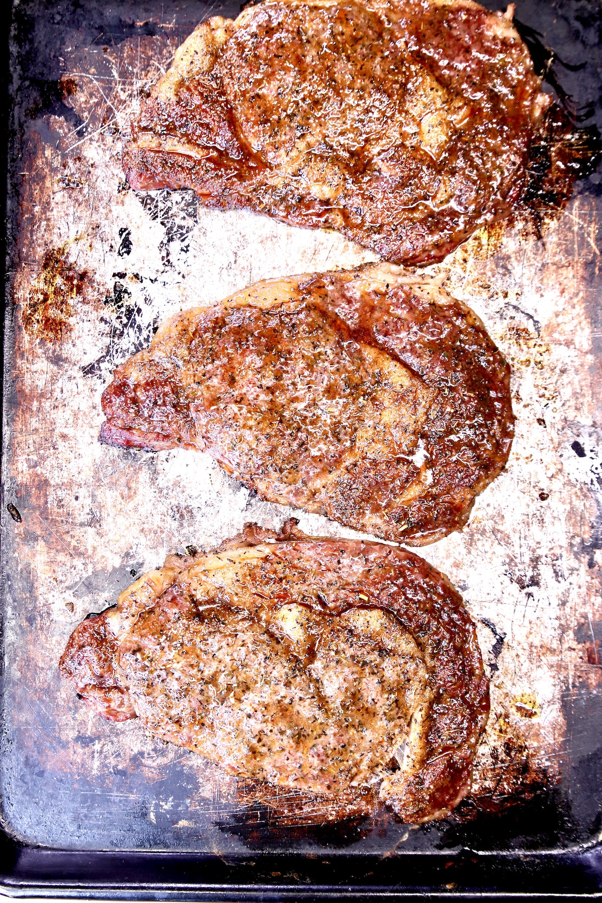 3 grilled ribeye steaks on a baking sheet.