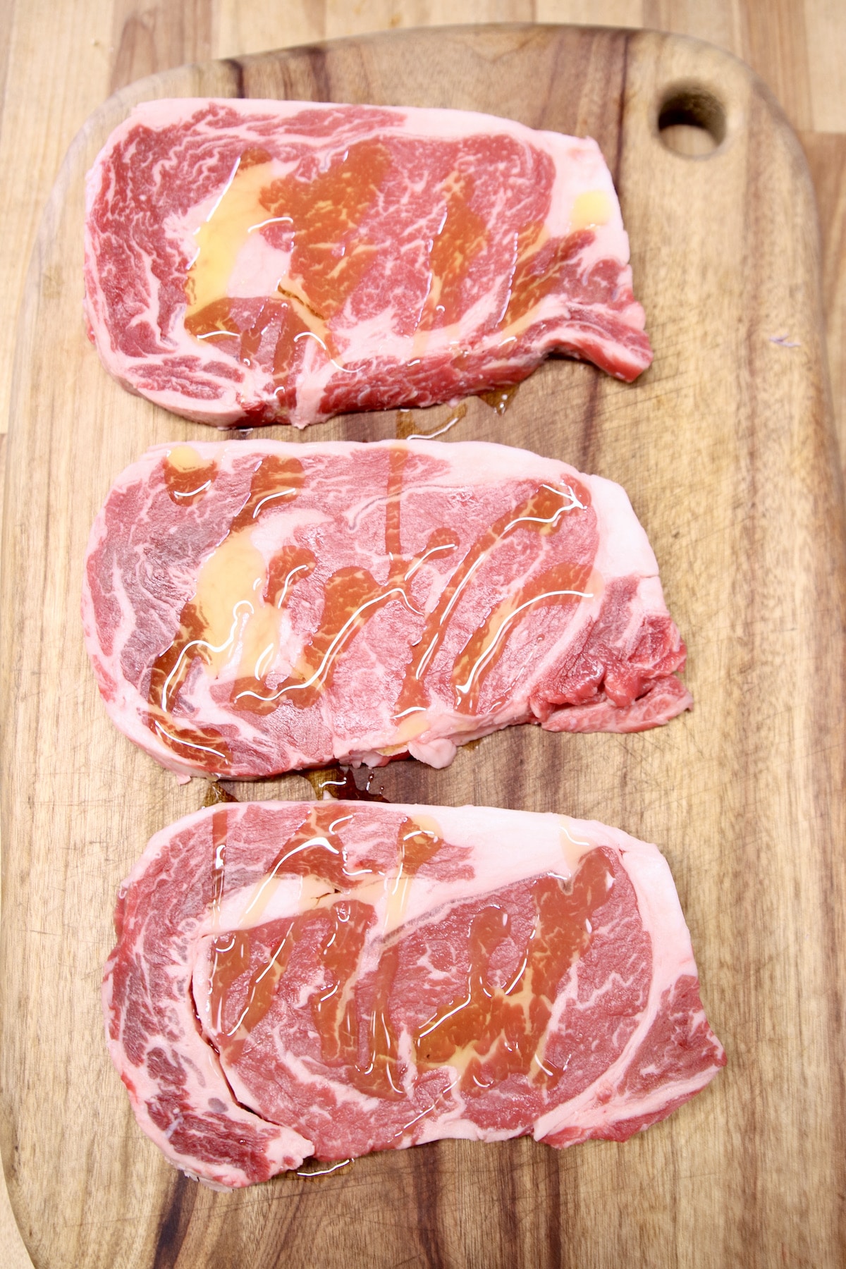 3 raw ribeyes drizzled with olive oil