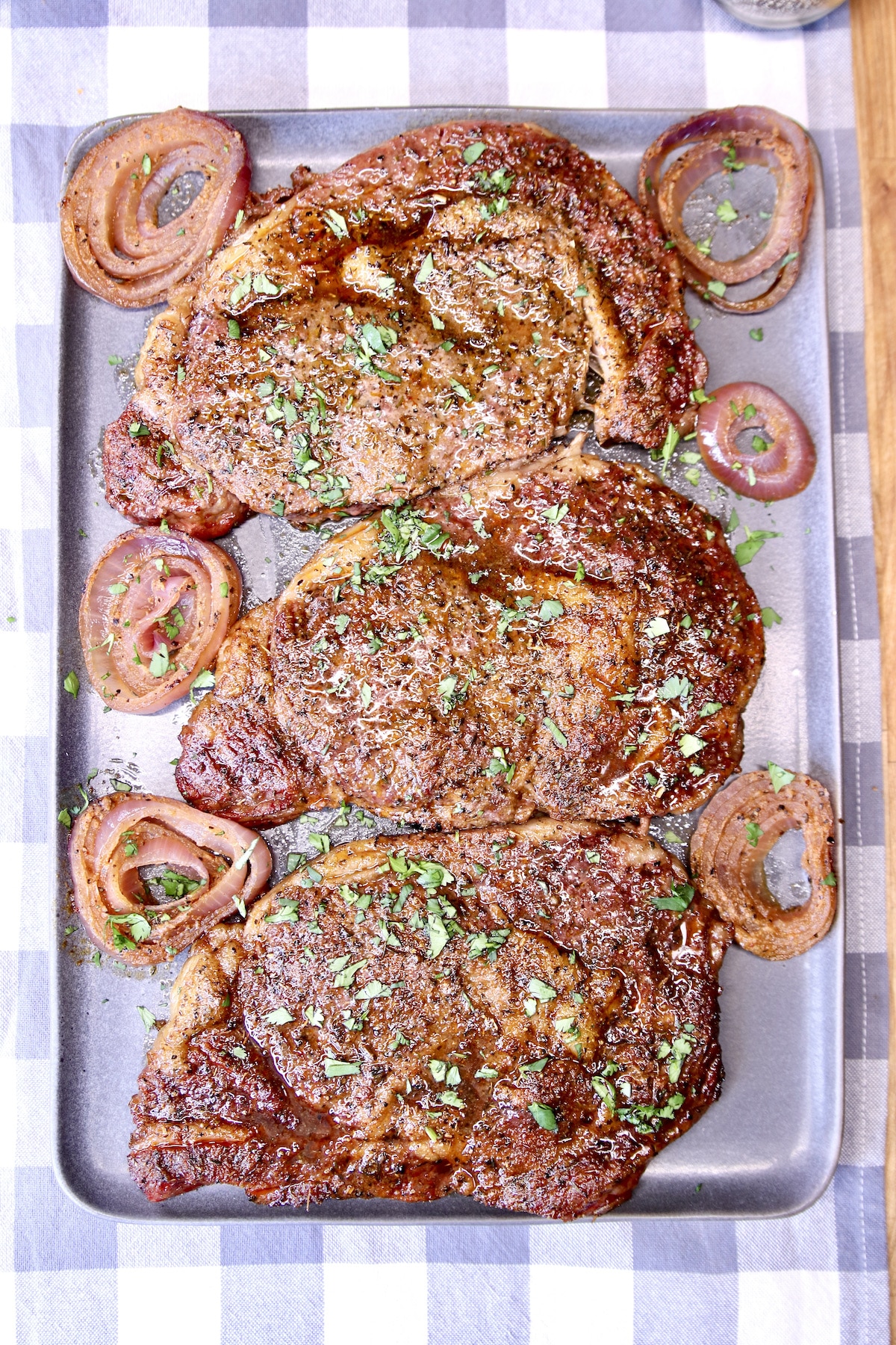 Grilled ribeye steaks with red onion slices on a gray platter.