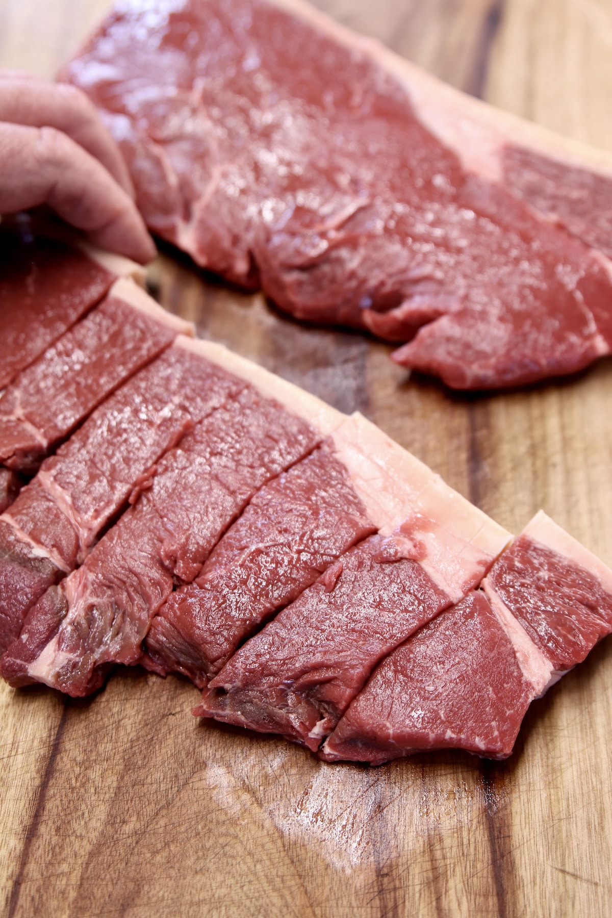 slicing raw sirloin steak on a cutting board.
