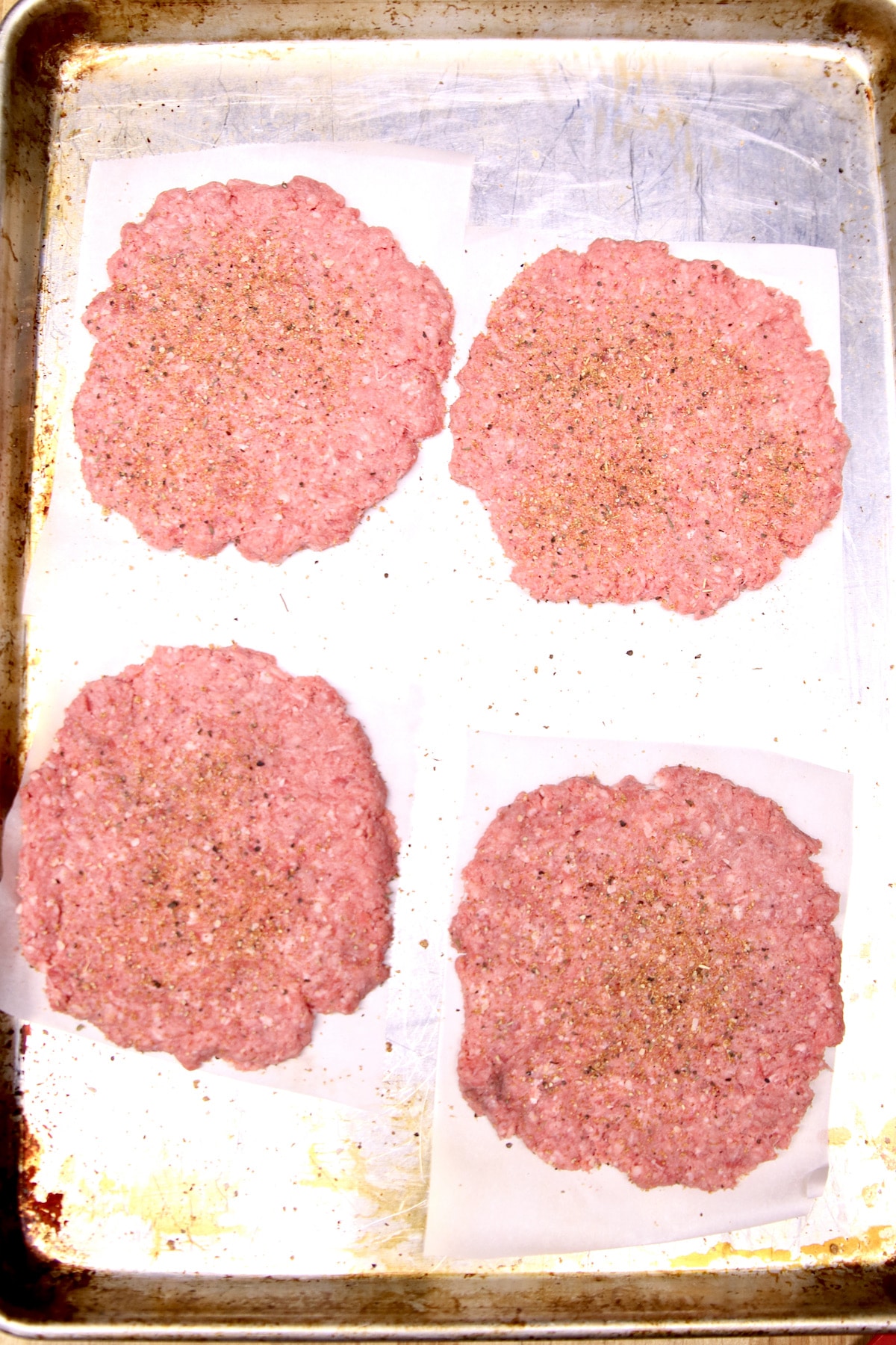 4 ground beef patties on a sheet pan.