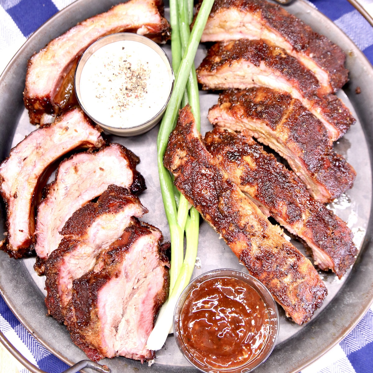 Platter with sliced baby back ribs, green onions, 2 bowls of sauce.