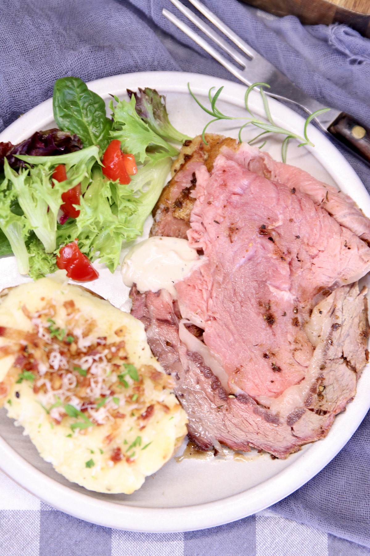 Plate of sliced prime rib, baked potato, salad.