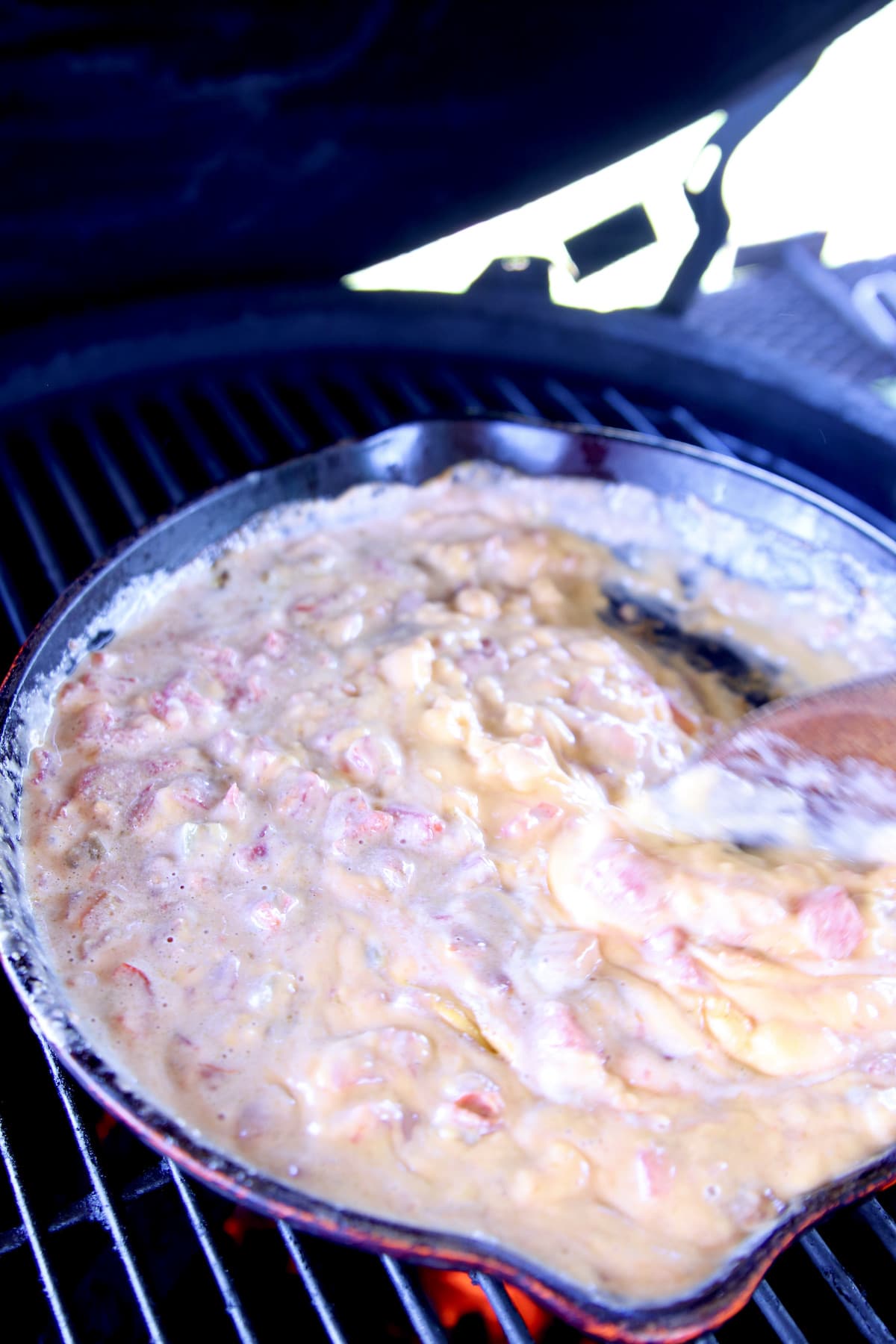 stirring cheese dip on a grill in a skillet.