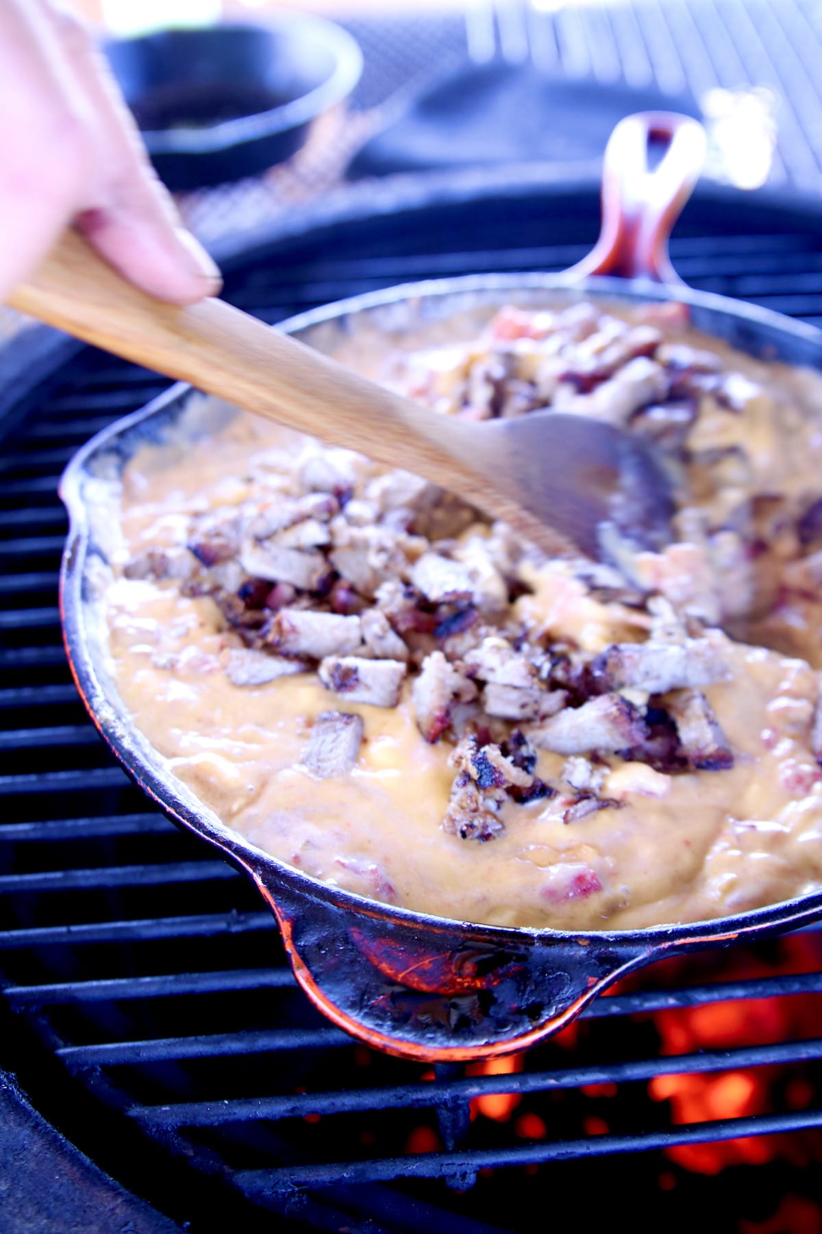 Stirring brisket into queso on a grill in a skillet.