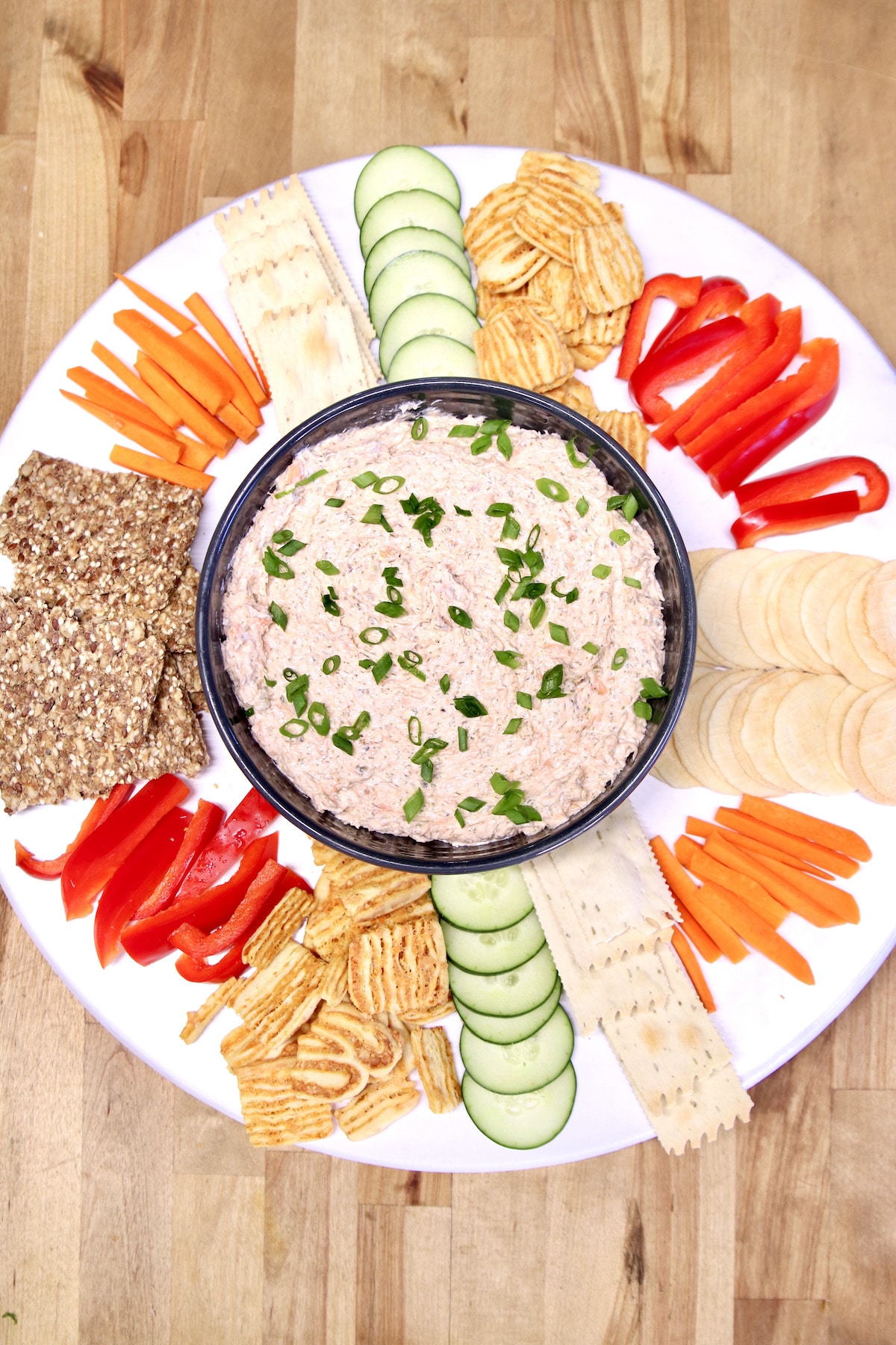 Platter of vegetables and crackers with salmon dip in center.