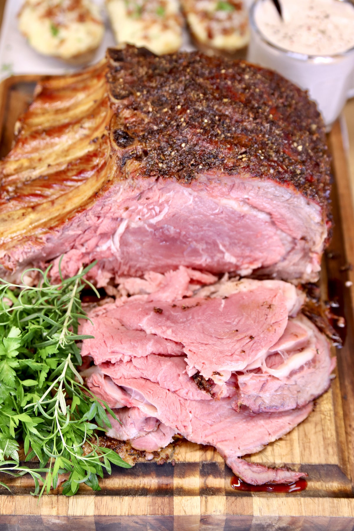 sliced standing rib roast on cutting board with fresh herb garnish.