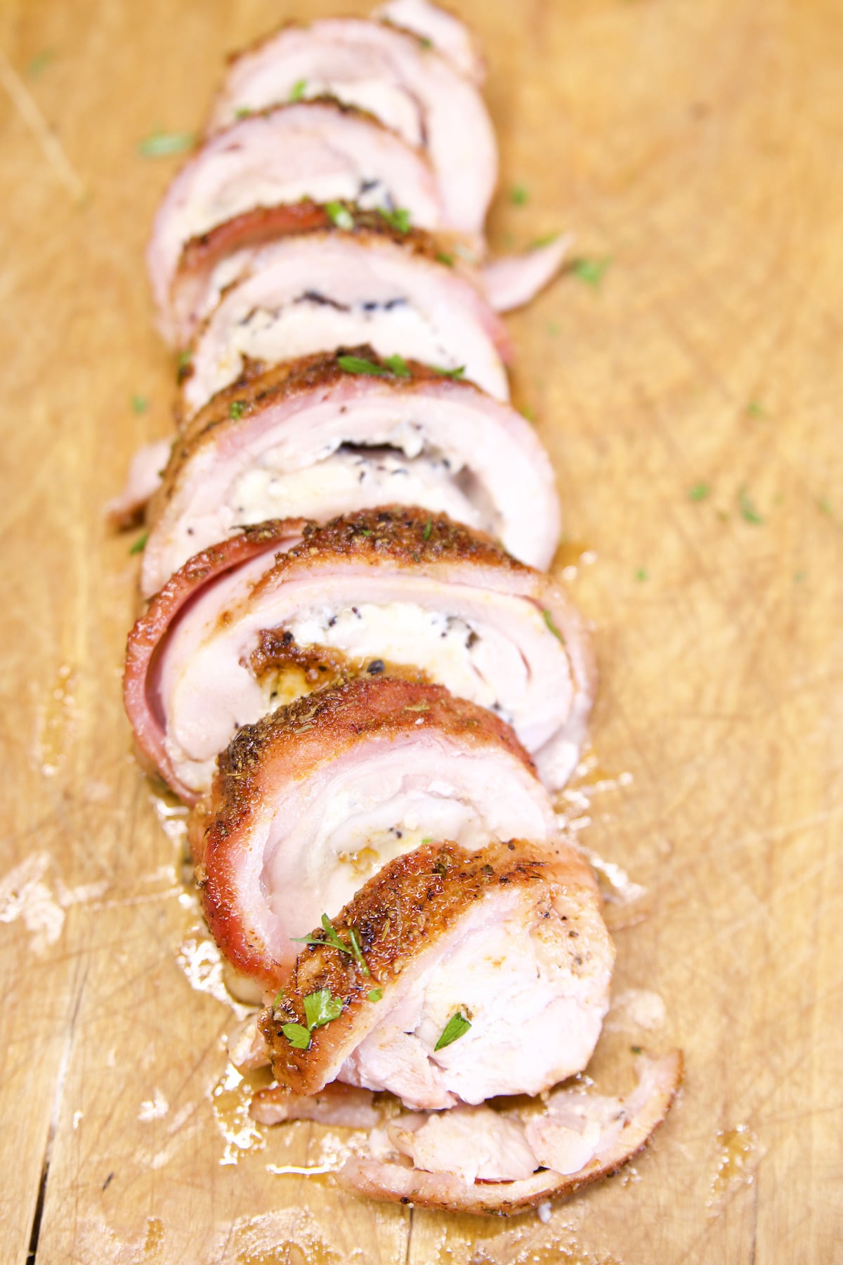 Sliced bacon wrapped stuffed chicken on a cutting board.