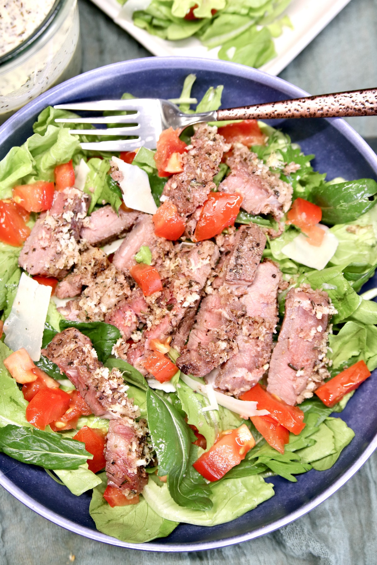 Bowl of salad topped with sliced steak.