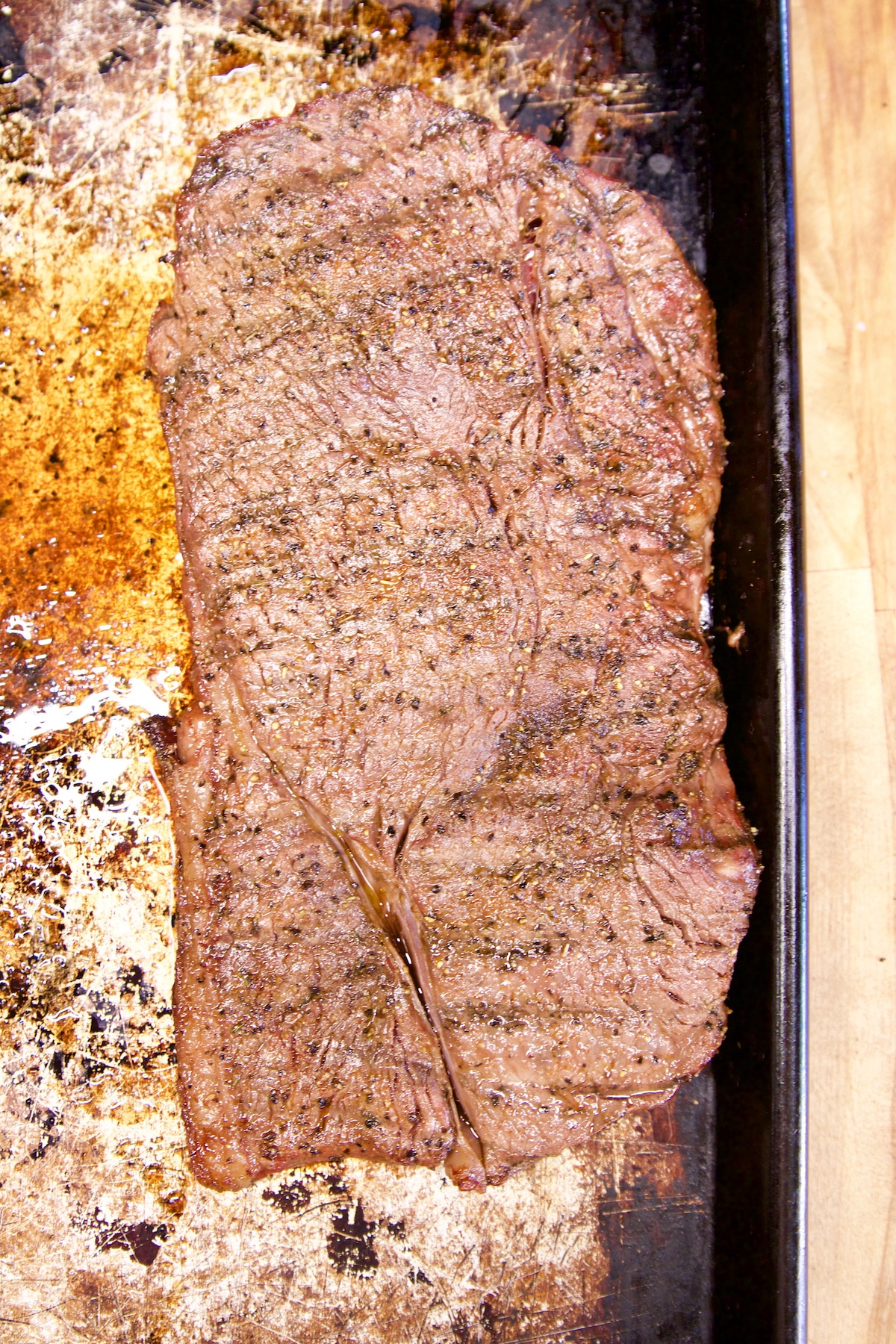 Grilled steak resting on a rimmed baking sheet.