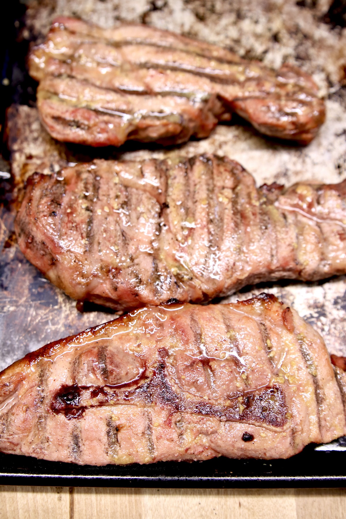 3 grilled pork steaks on a sheet pan.