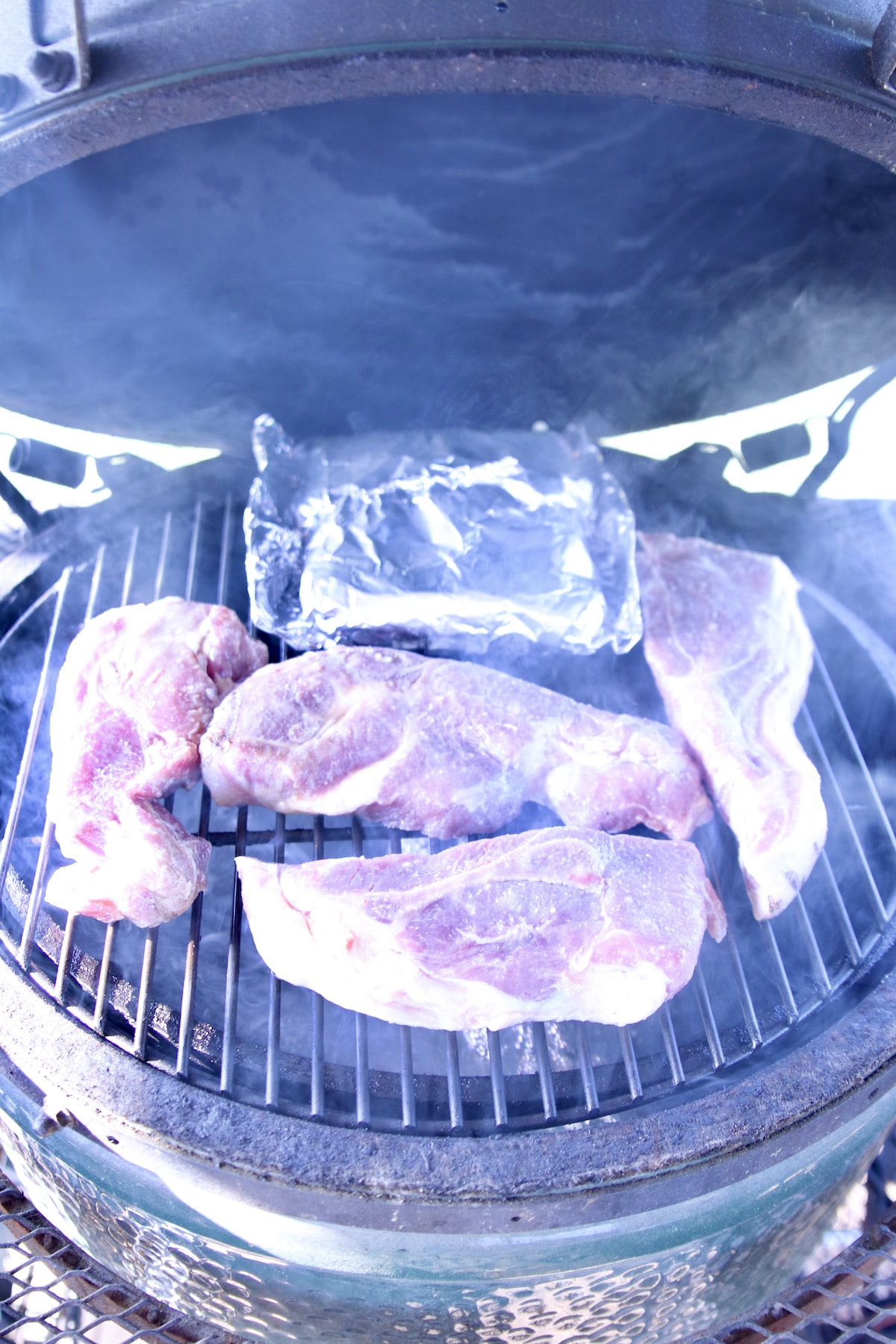 pork steaks on a grill with foil packet corn.