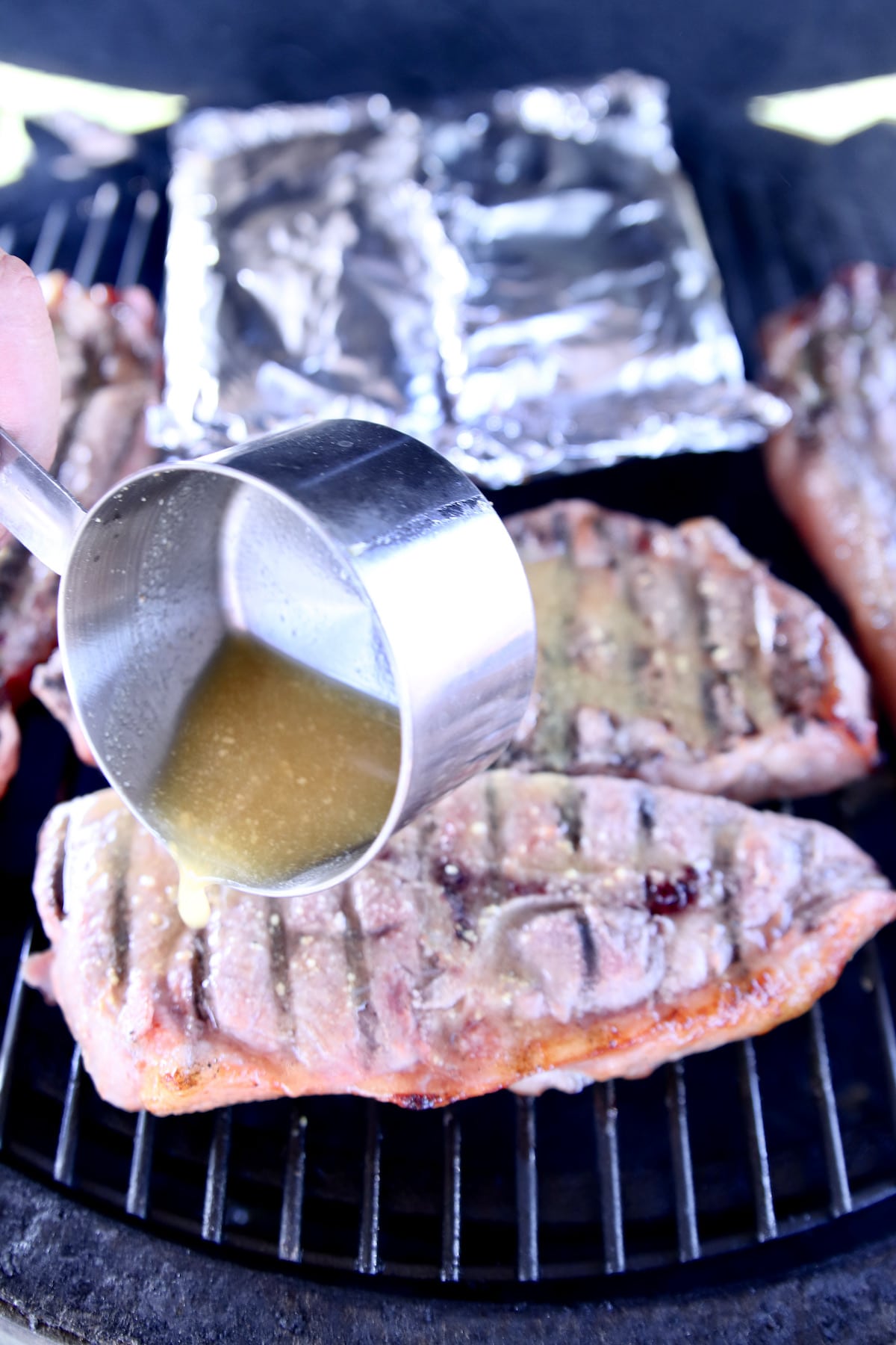 Pouring marinade over grilled pork steaks.