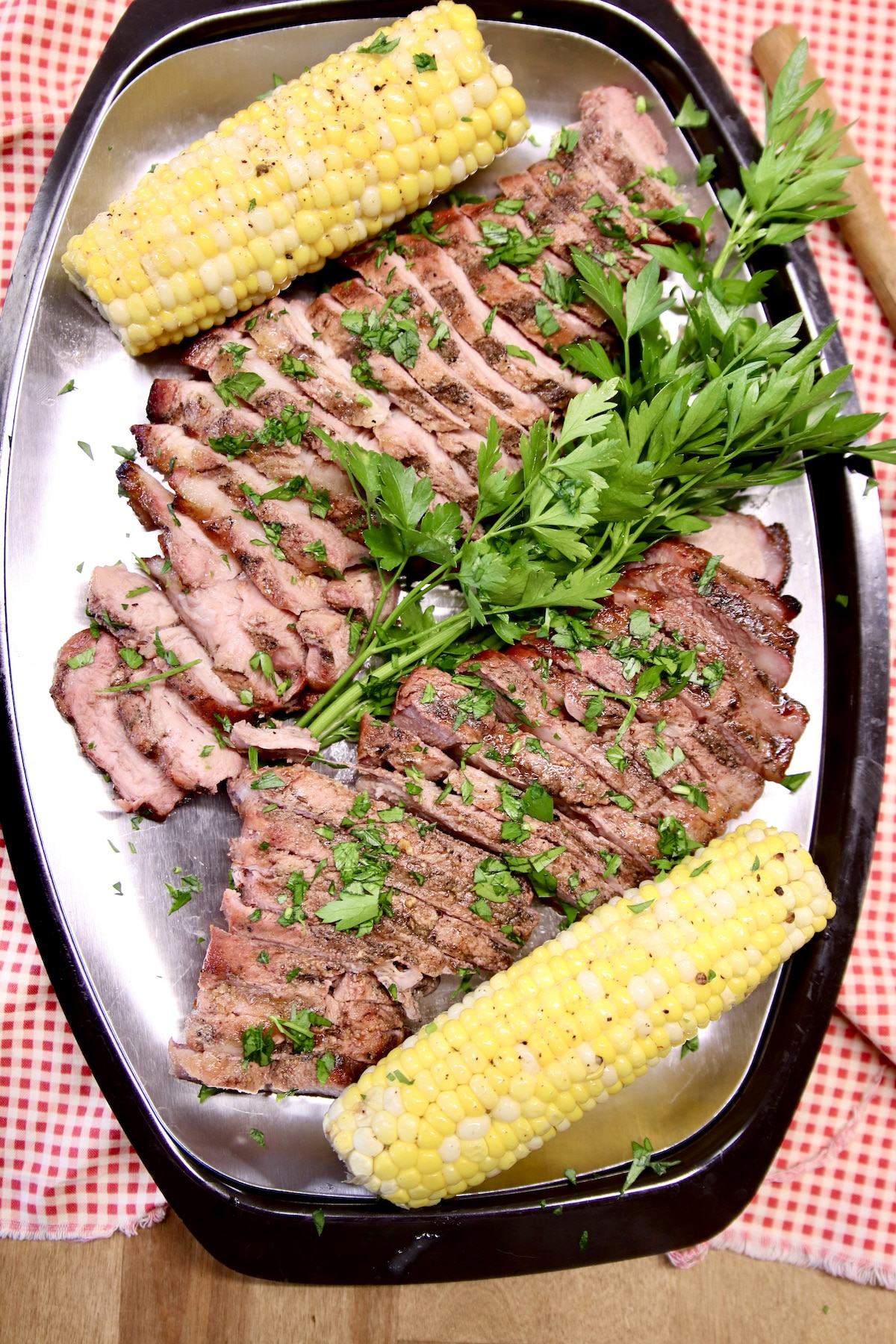 Platter of grilled pork steaks with 2 corn cobs.