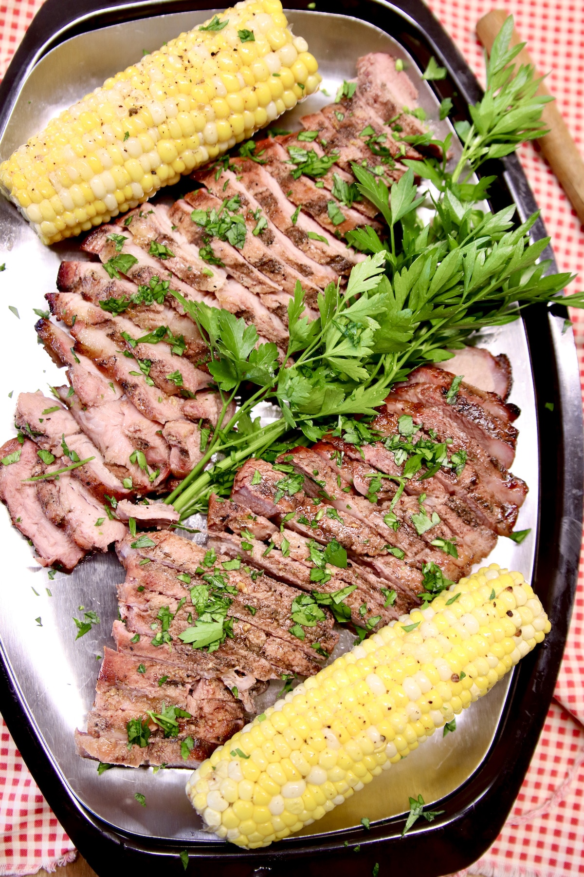 Platter of sliced pork steak with 2 corns on the cob.