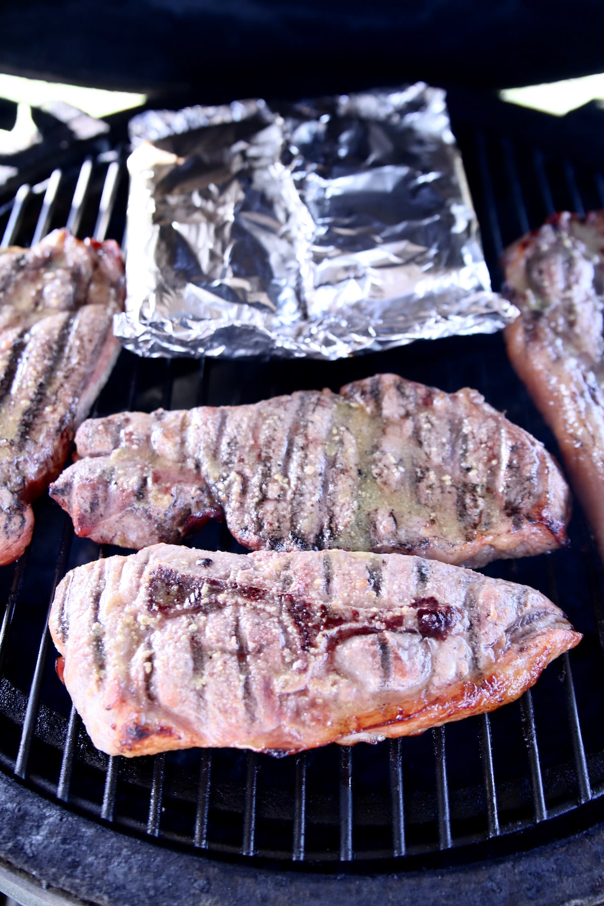 Pork steaks on a grill with foil packet corn.