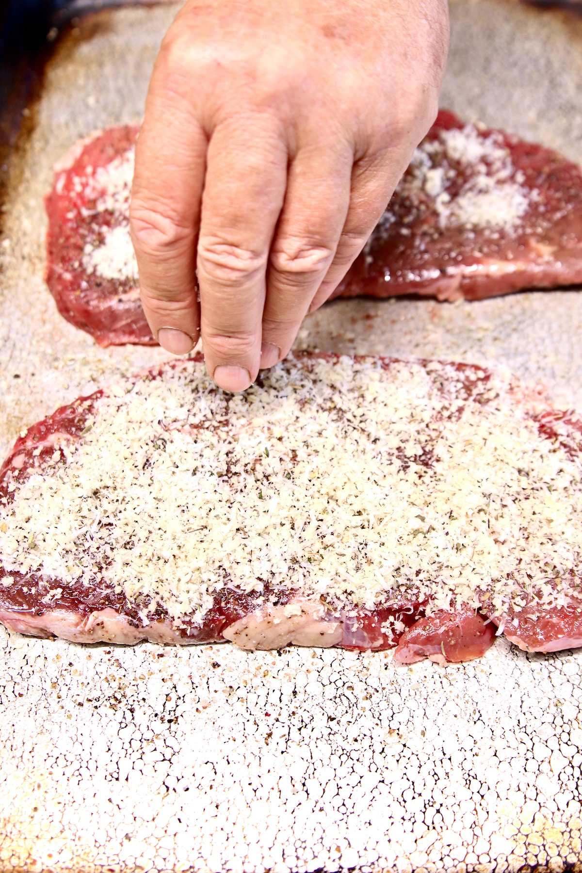 Sprinkling parmesan crust over sirloin steak.