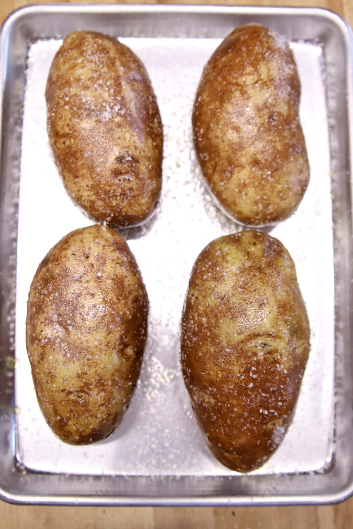4 russet potatoes on a baking sheet.