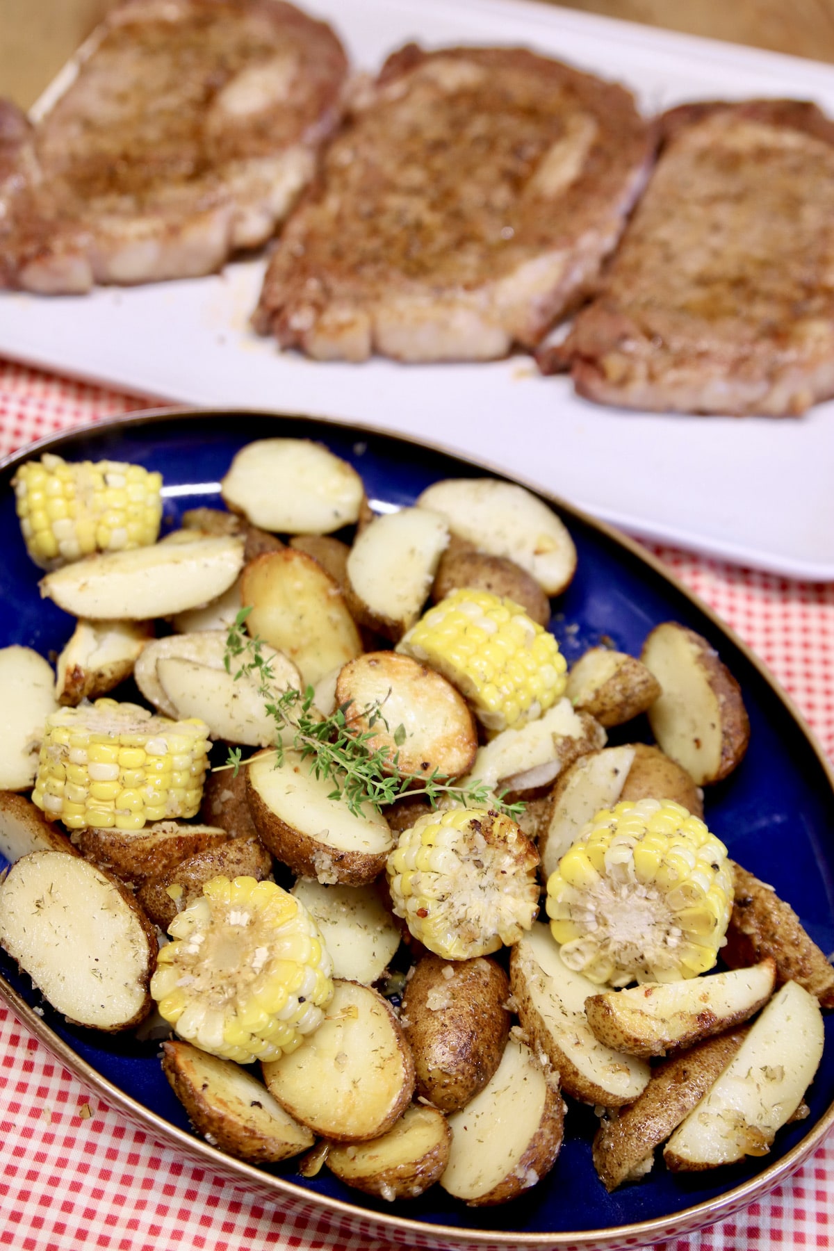 Platter of potatoes and corn with platter of grilled steaks.