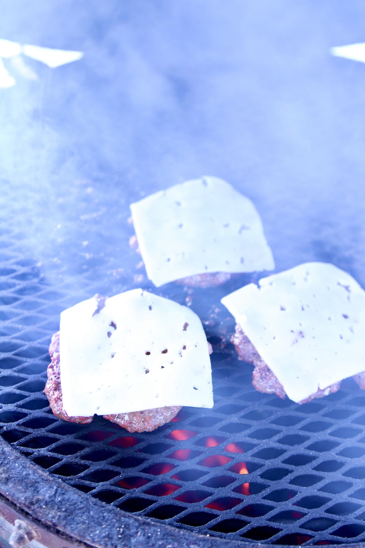 Swiss slices over burger patties on grill.