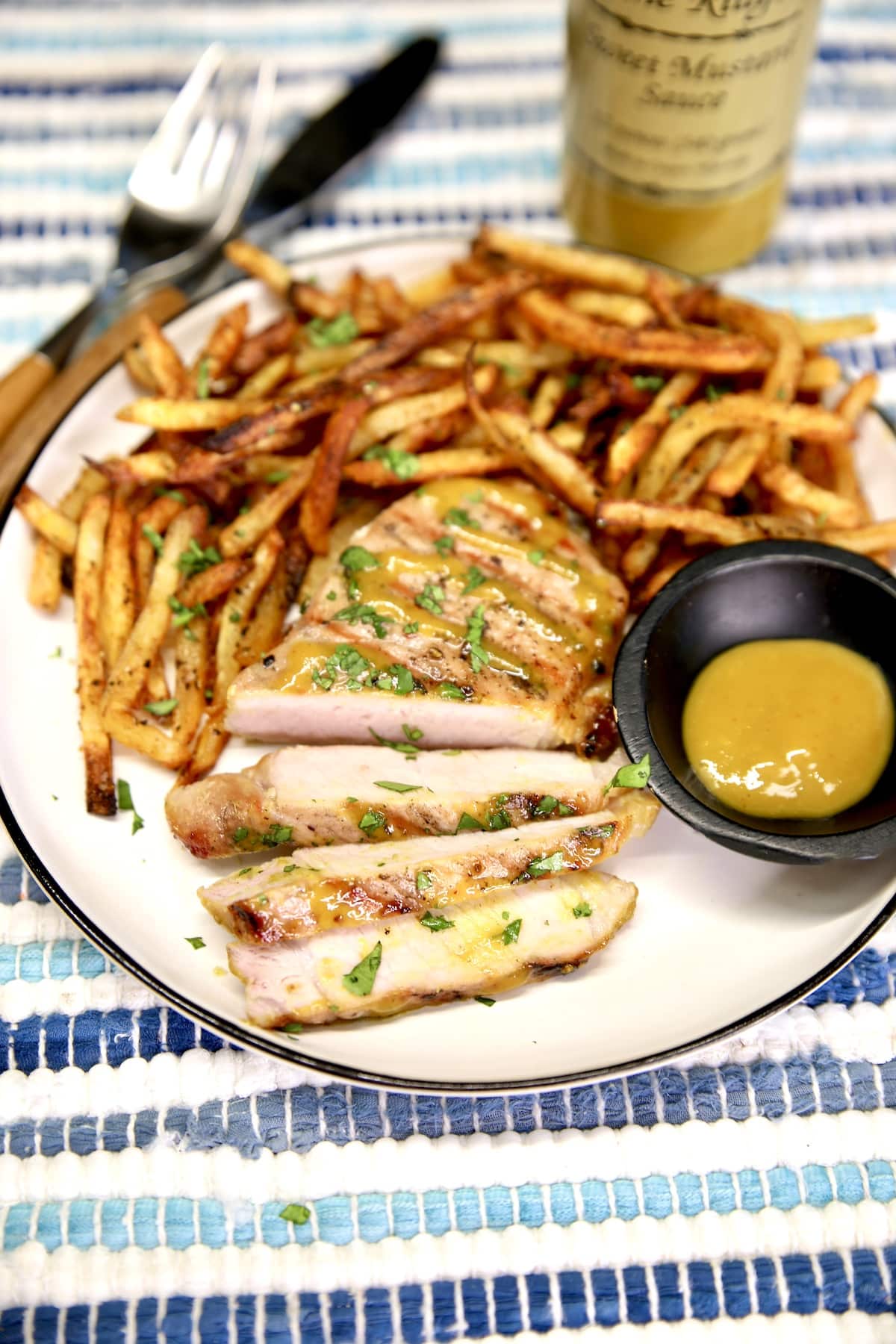 Mustard glazed pork chop on a plate with fries and mustard sauce.