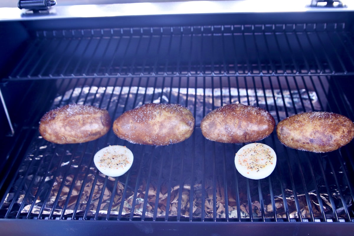 Pellet grill with 4 baked potatoes, onion.