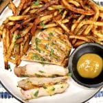 Mustard pork chop on a plate, partially sliced with mustard and fries.