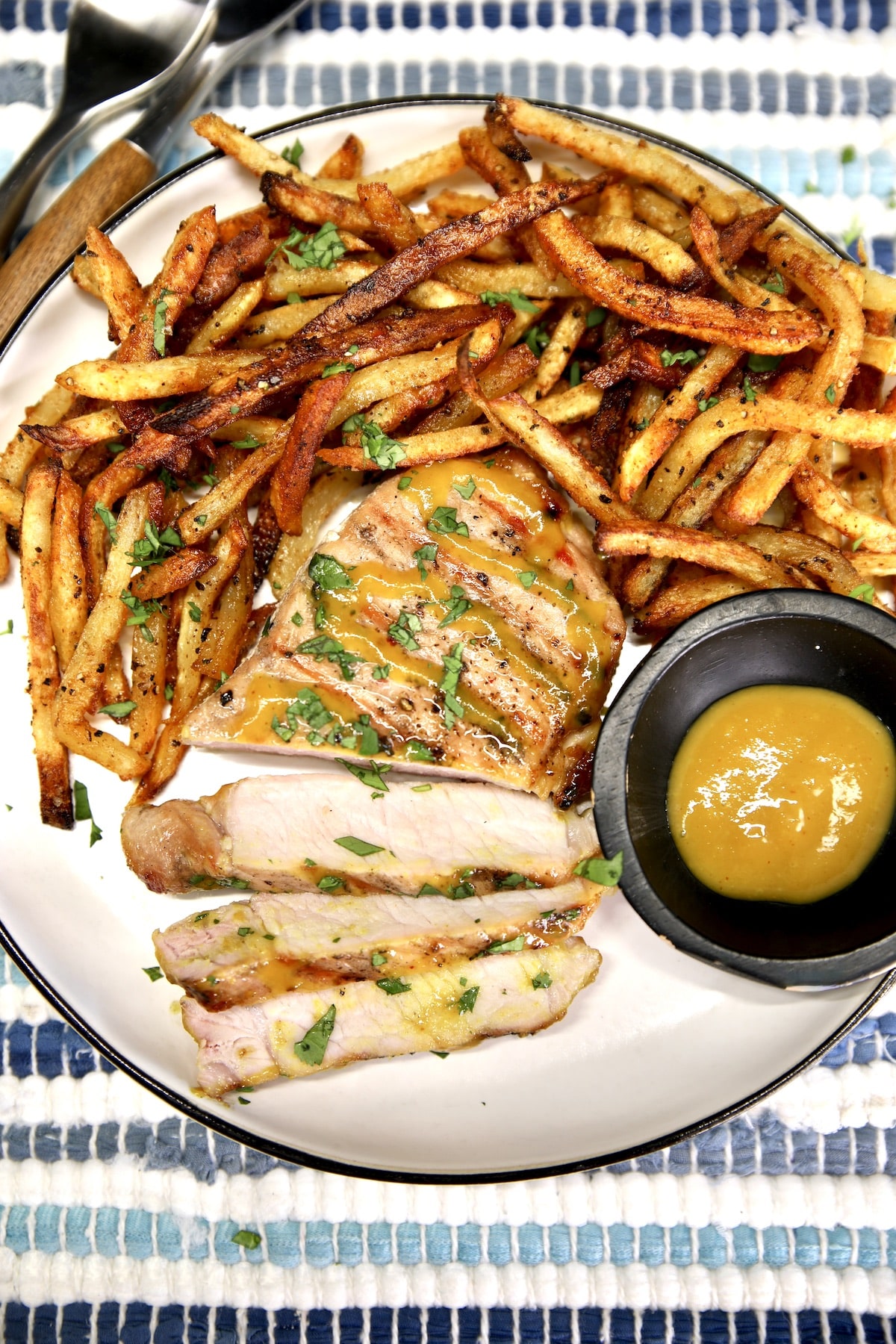Plate of fries with pork chop, partially sliced.