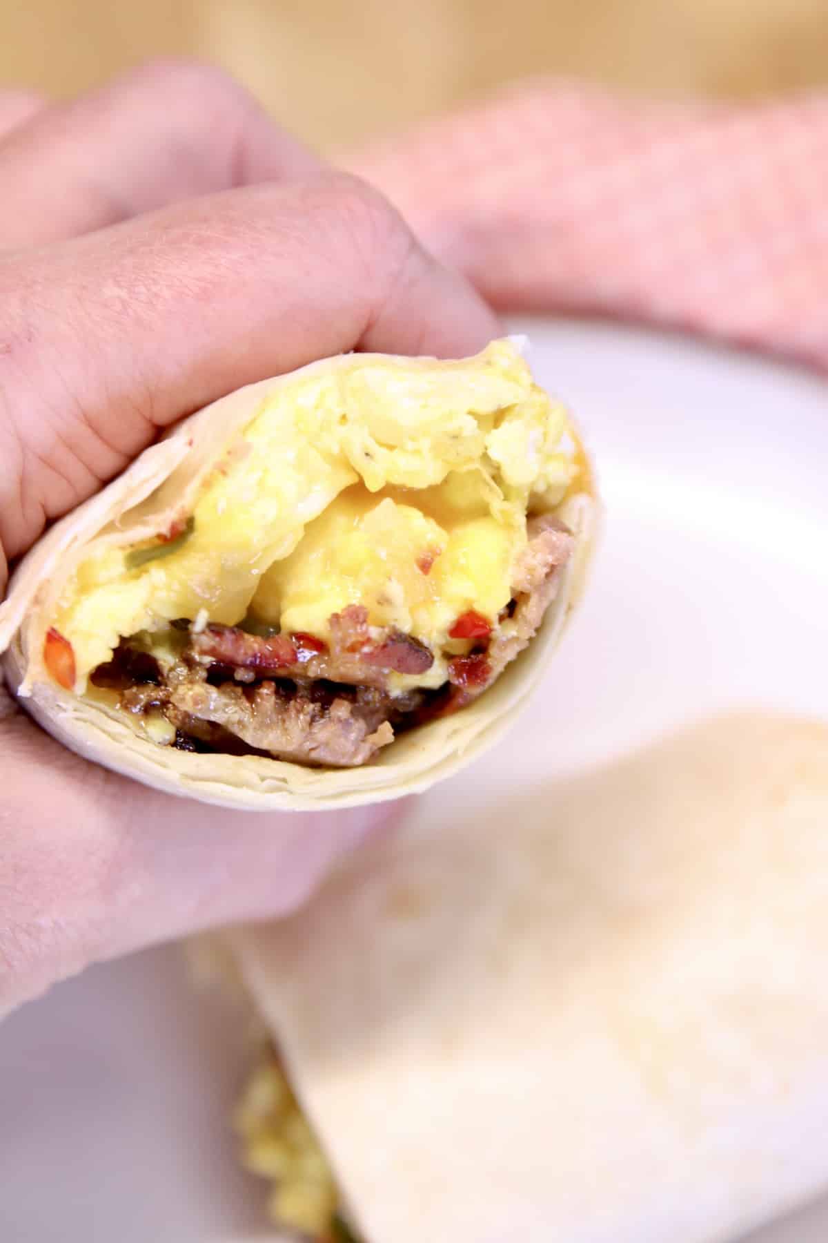 Hand holding egg and cheese burrito.