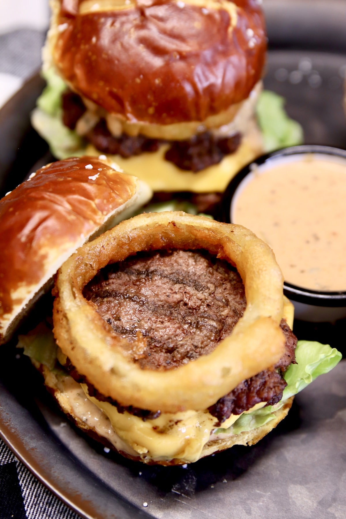 Closeup of grilled cheeseburger slider with onion ring on top.