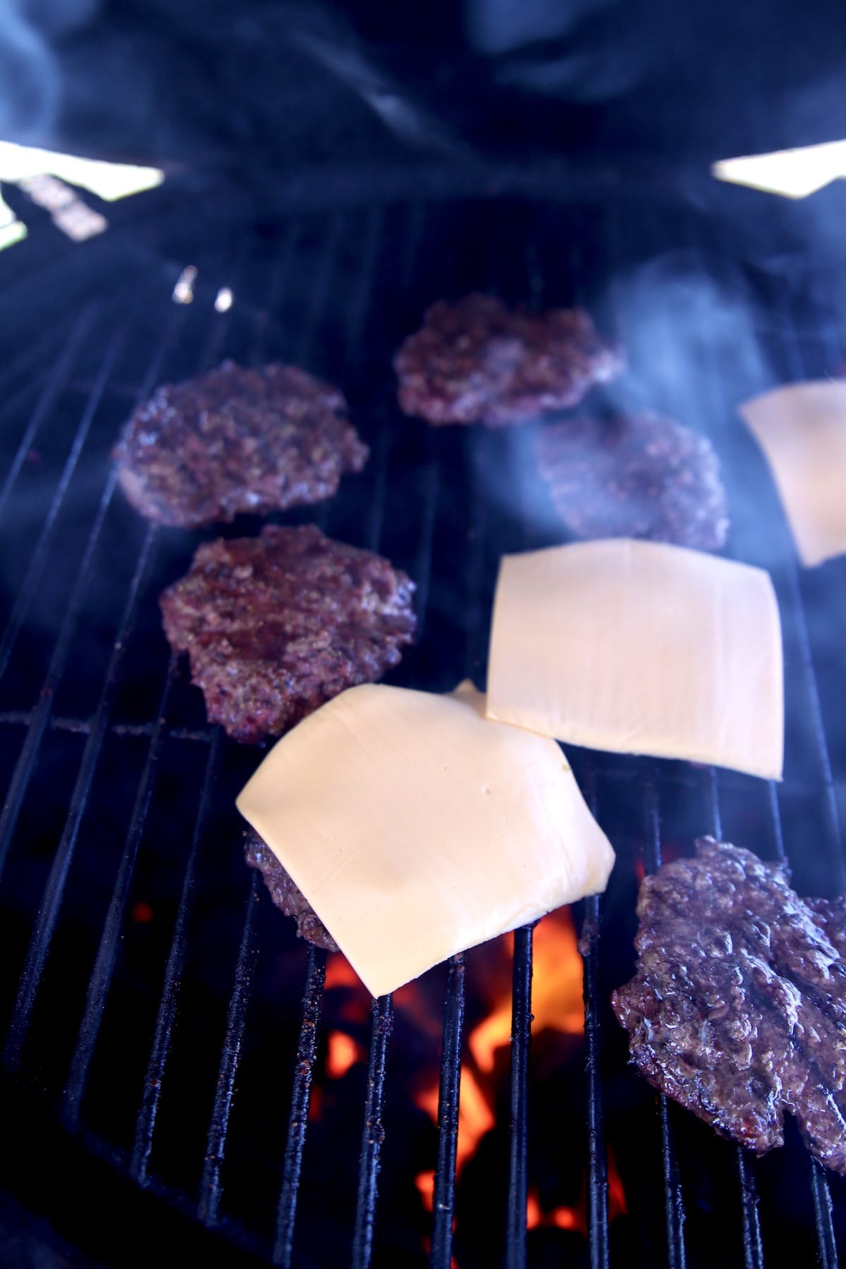American cheese slices on burger patties on a grill.