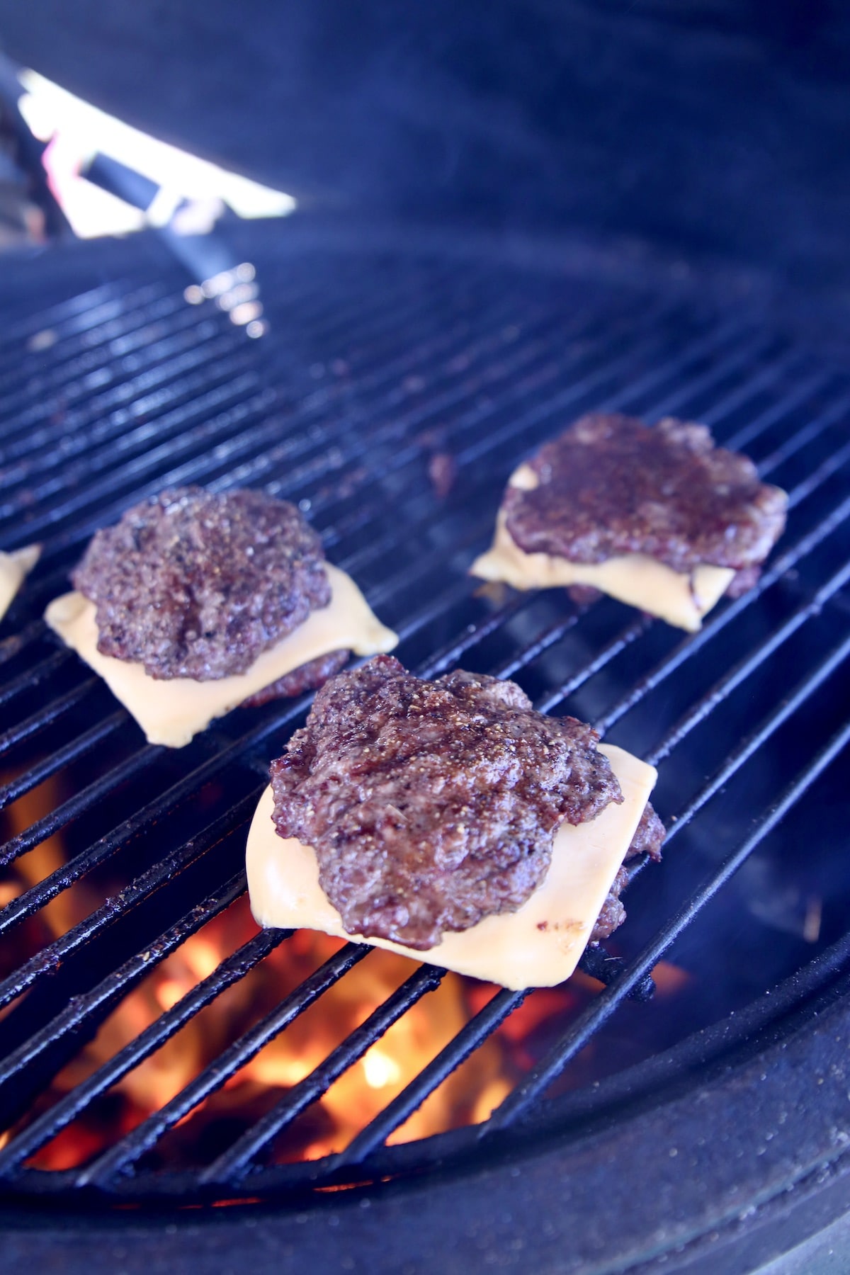 Burger sliders with cheese on a grill.