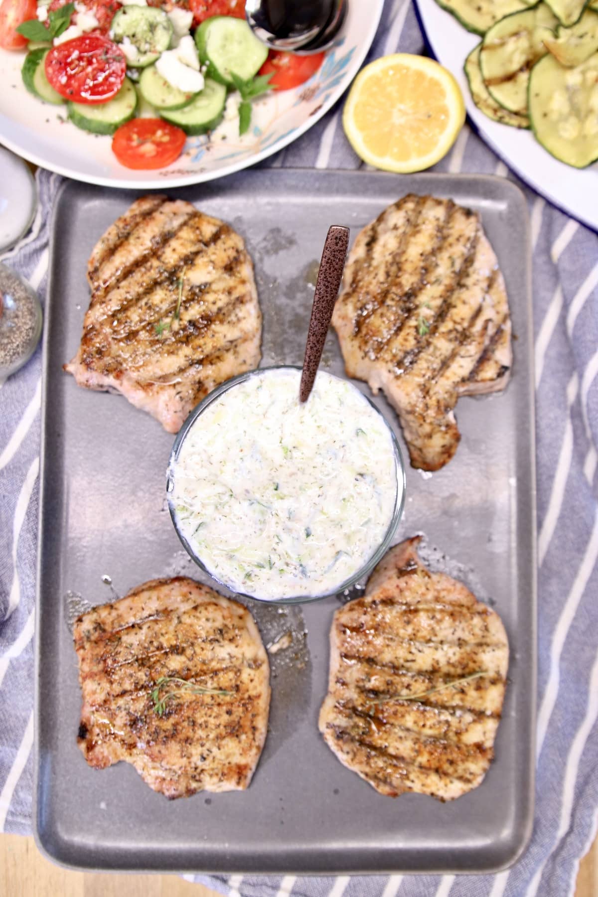 Grilled pork chops on a platter with tzatziki sauce.