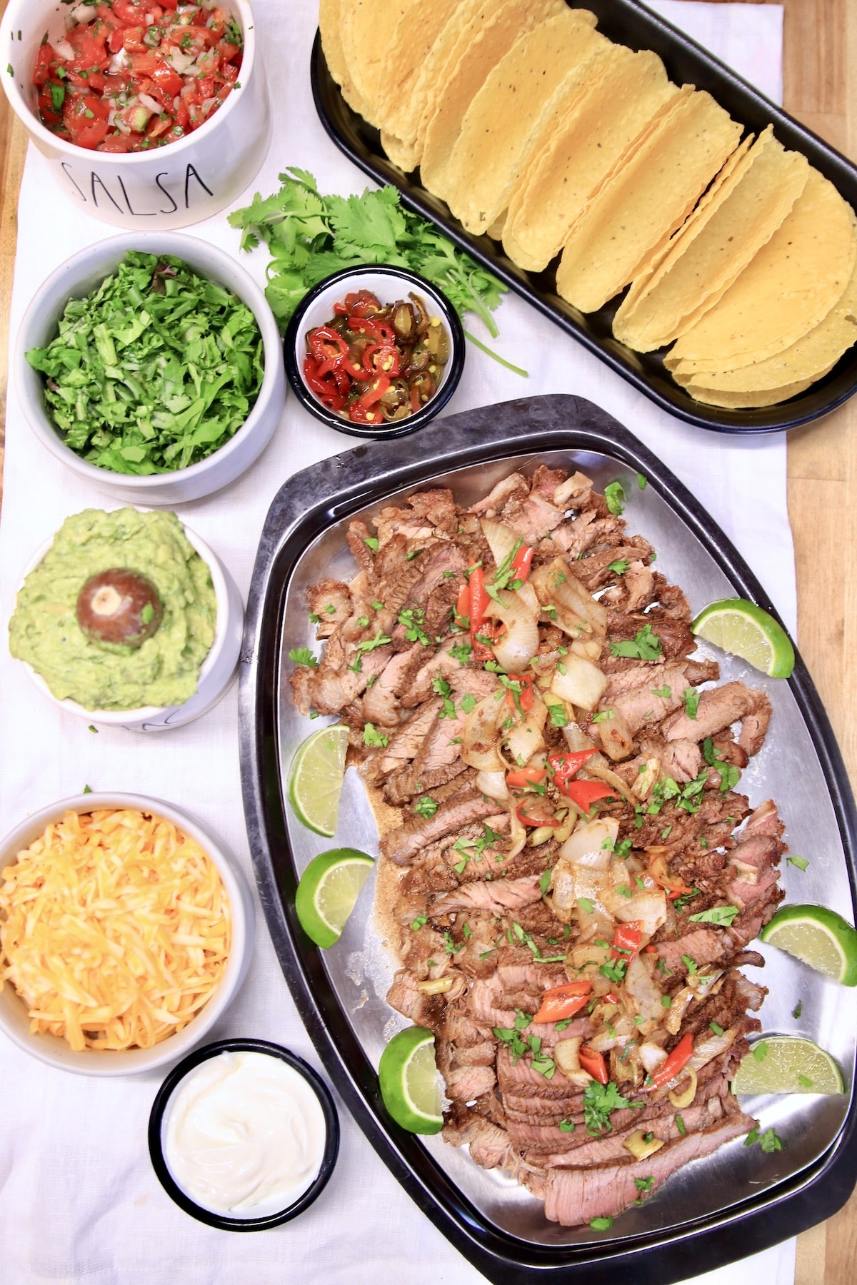 Platter of steak tacos with toppings and shells.