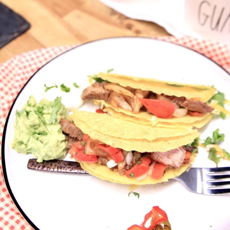2 steak tacos on a plate with a fork and guacamole.