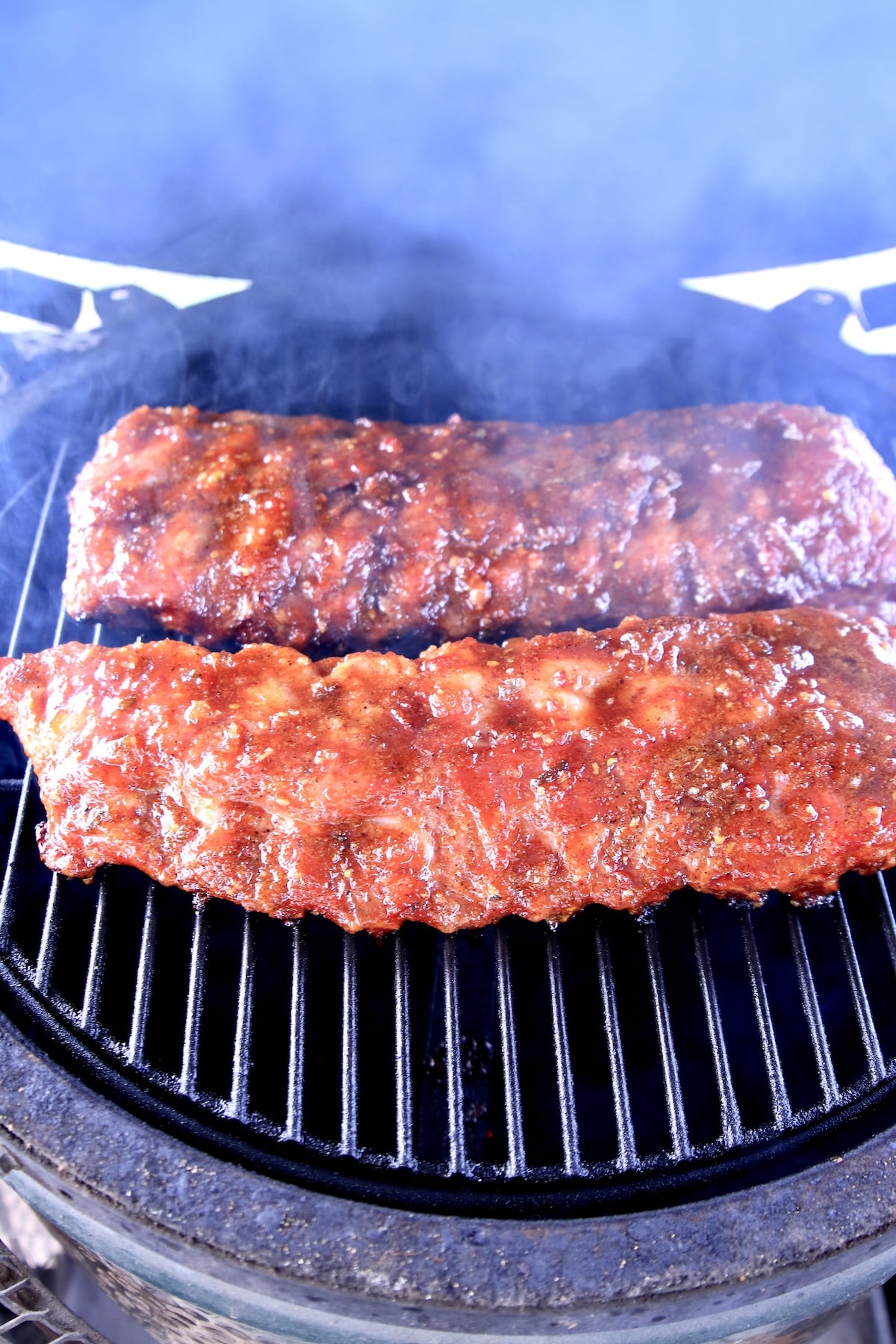 BBQ baby back ribs - 2 racks on a grill with smoke.